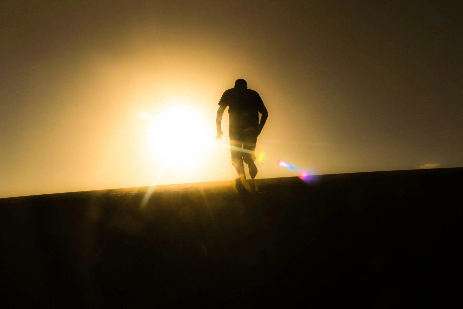A man is walking towards the sun at sunset.