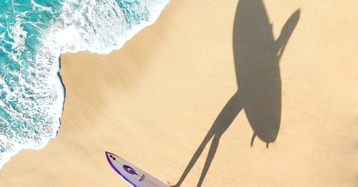 A shadow of a person holding a surfboard on a beach, perhaps on vacation.