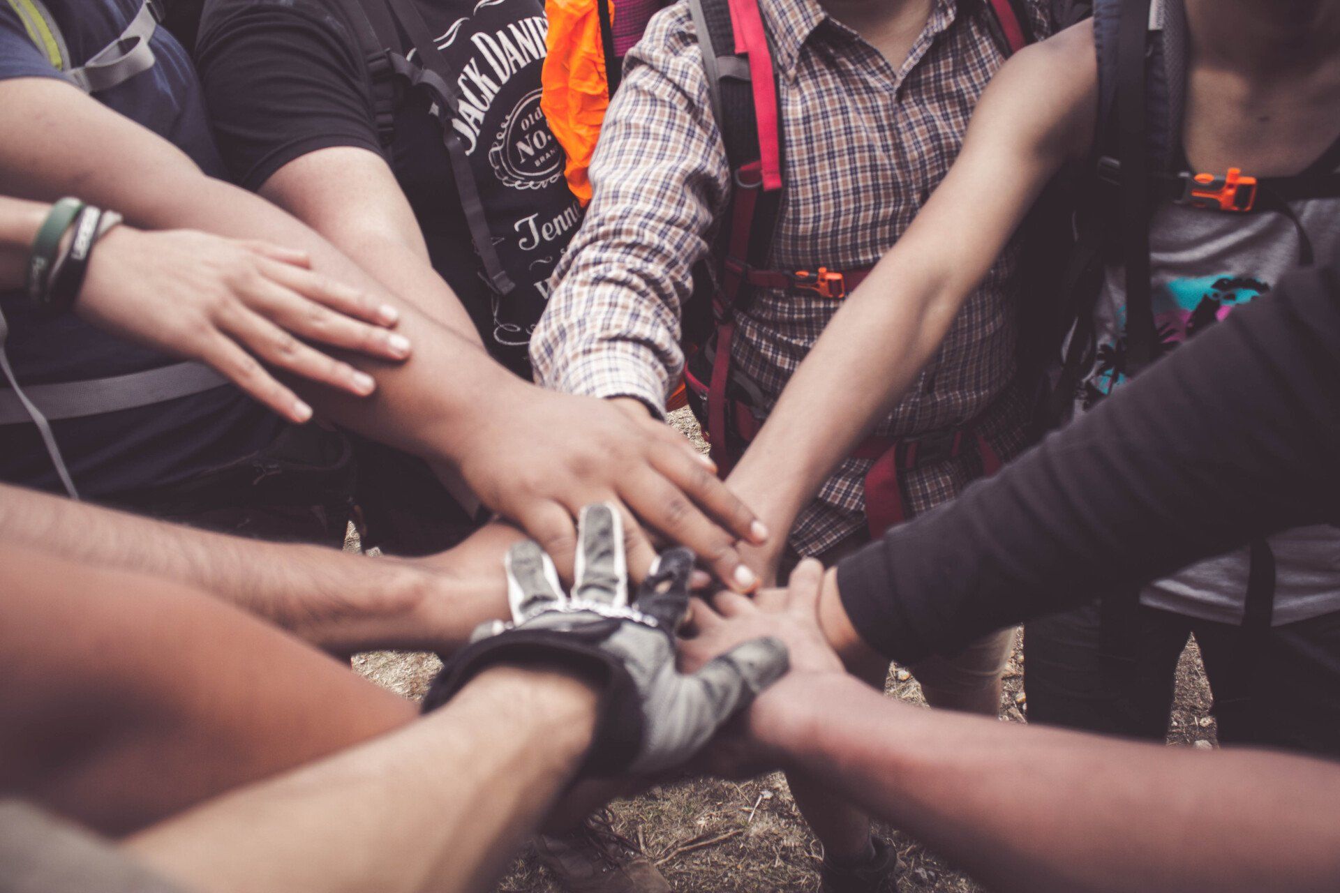A close-up of a group of people placing their hands together in a circle, signifying teamwork and unity.