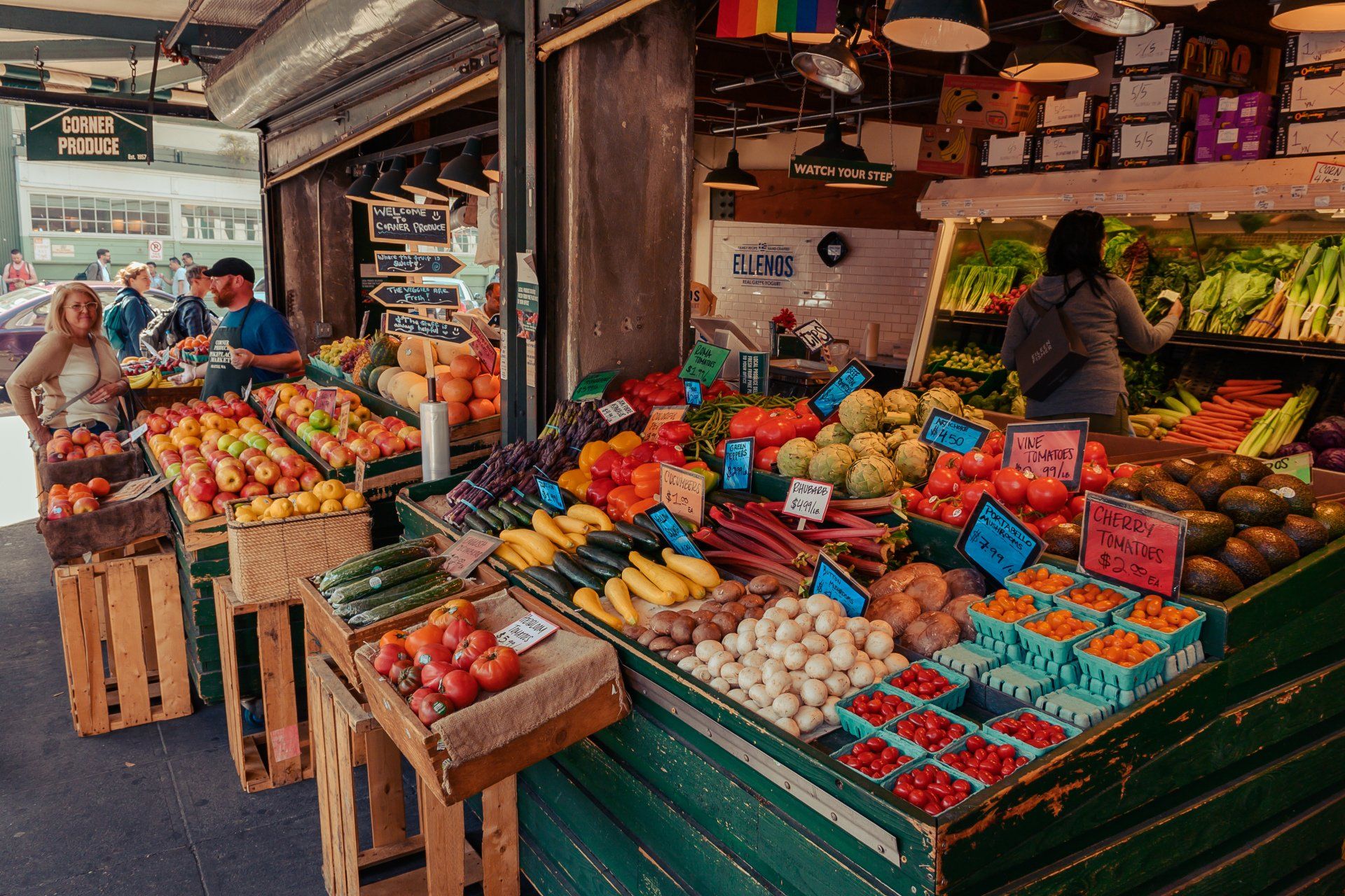 A woman is standing in front of a fruit and vegetable stand at a market.