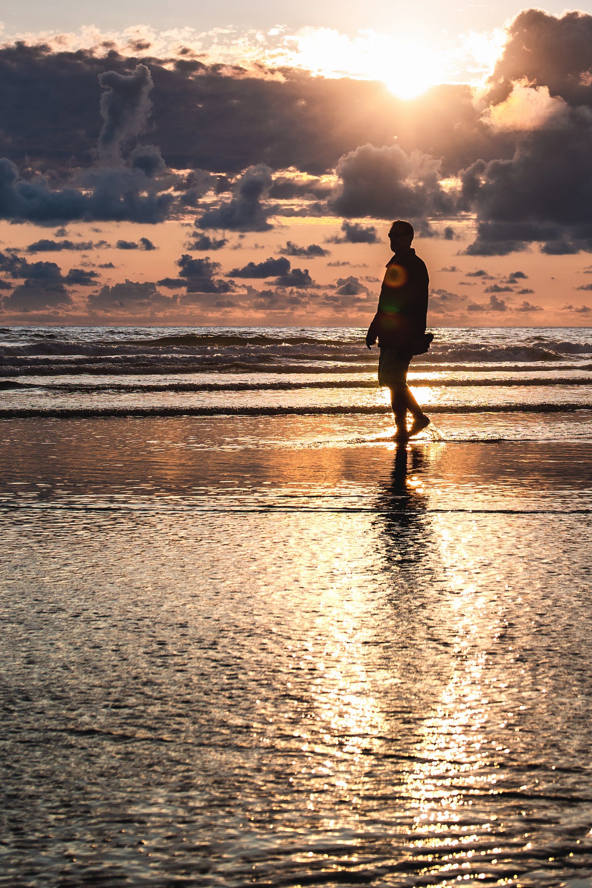 A man is walking on the beach at sunset.