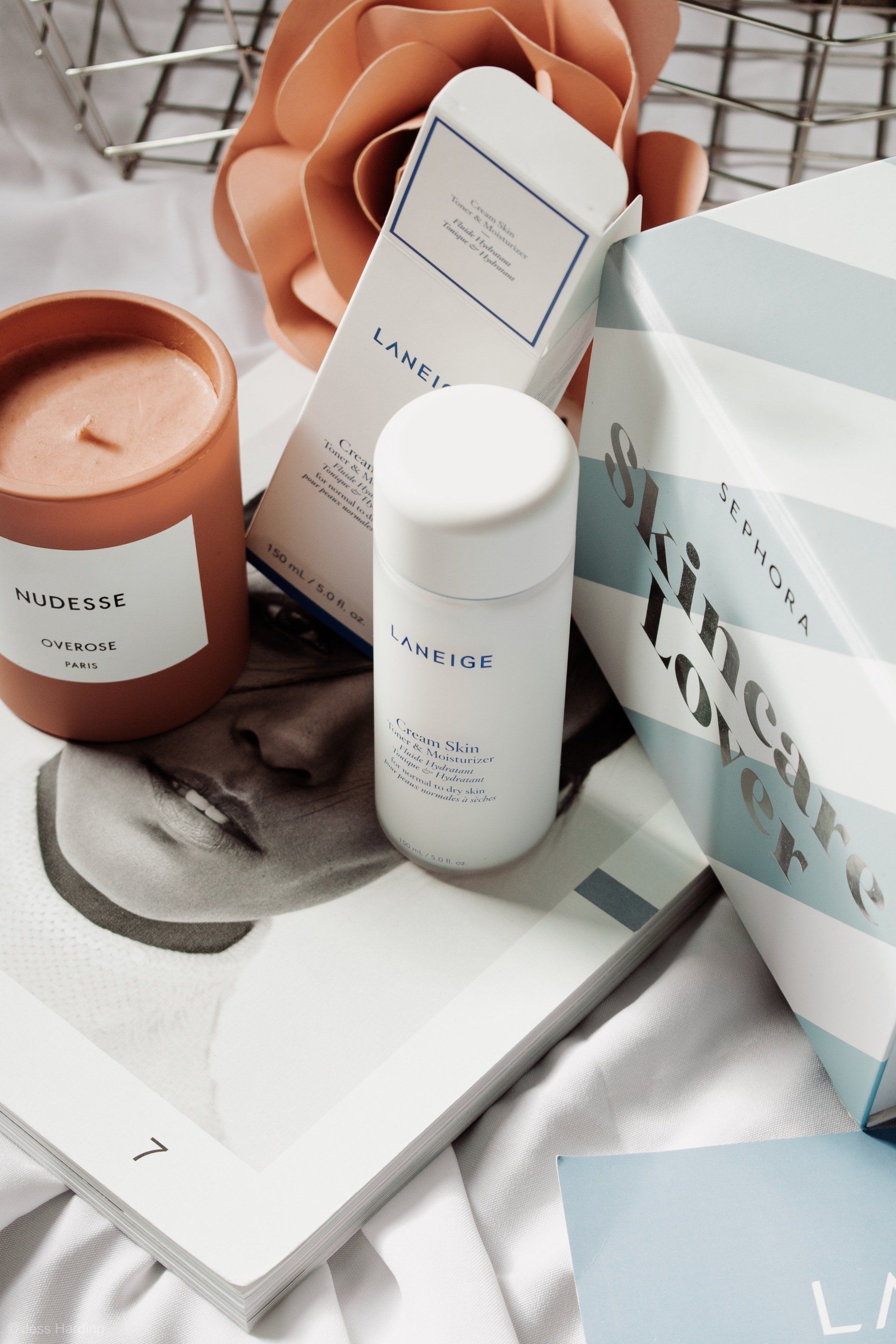Produtos de cuidados com a pele da Laneige, uma vela de terracota e uma sacola da Sephora estão dispostos sobre uma superfície com uma revista de moda.