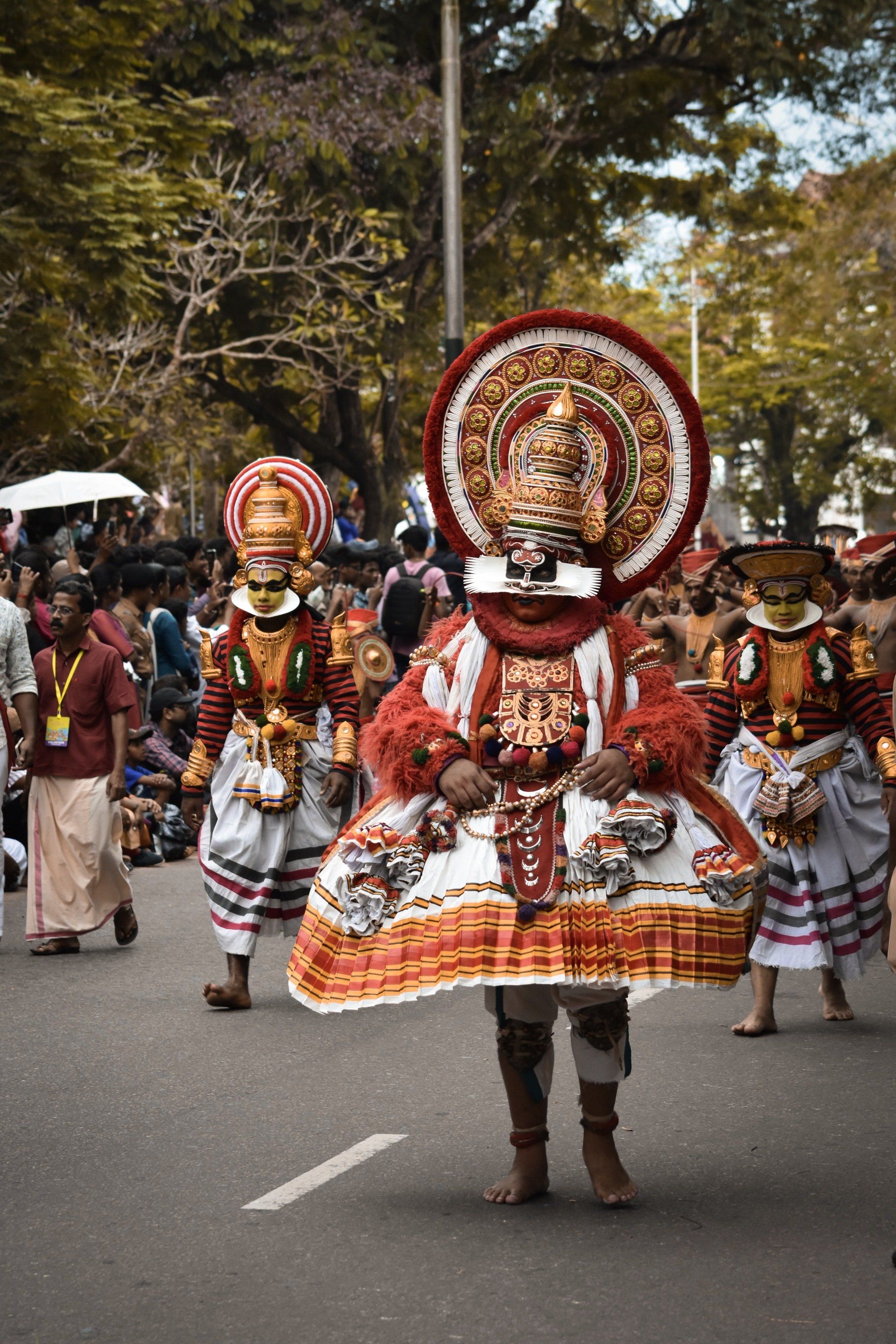 People in elaborate, red and white Kathakali costumes performing on a street. kerala