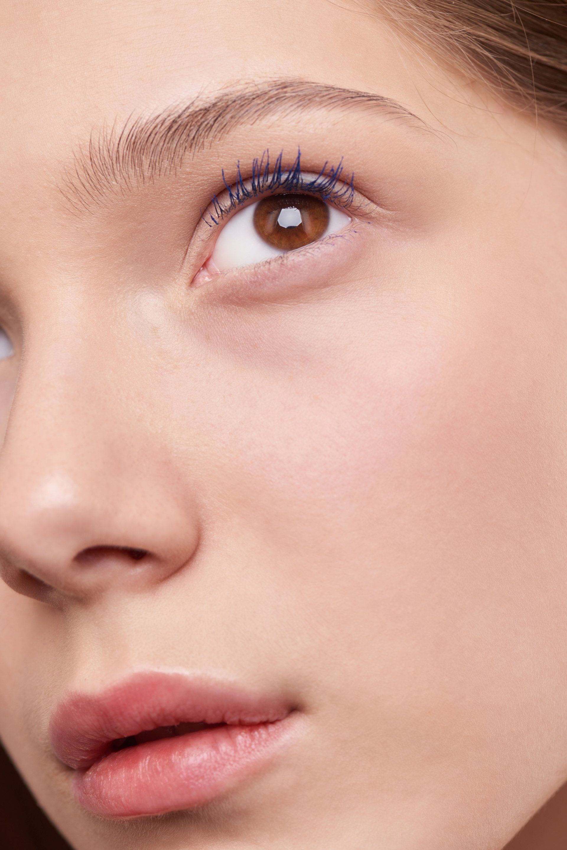 Close-up of a person with brown eyes, pink lips, and blue mascara, angled to the right.