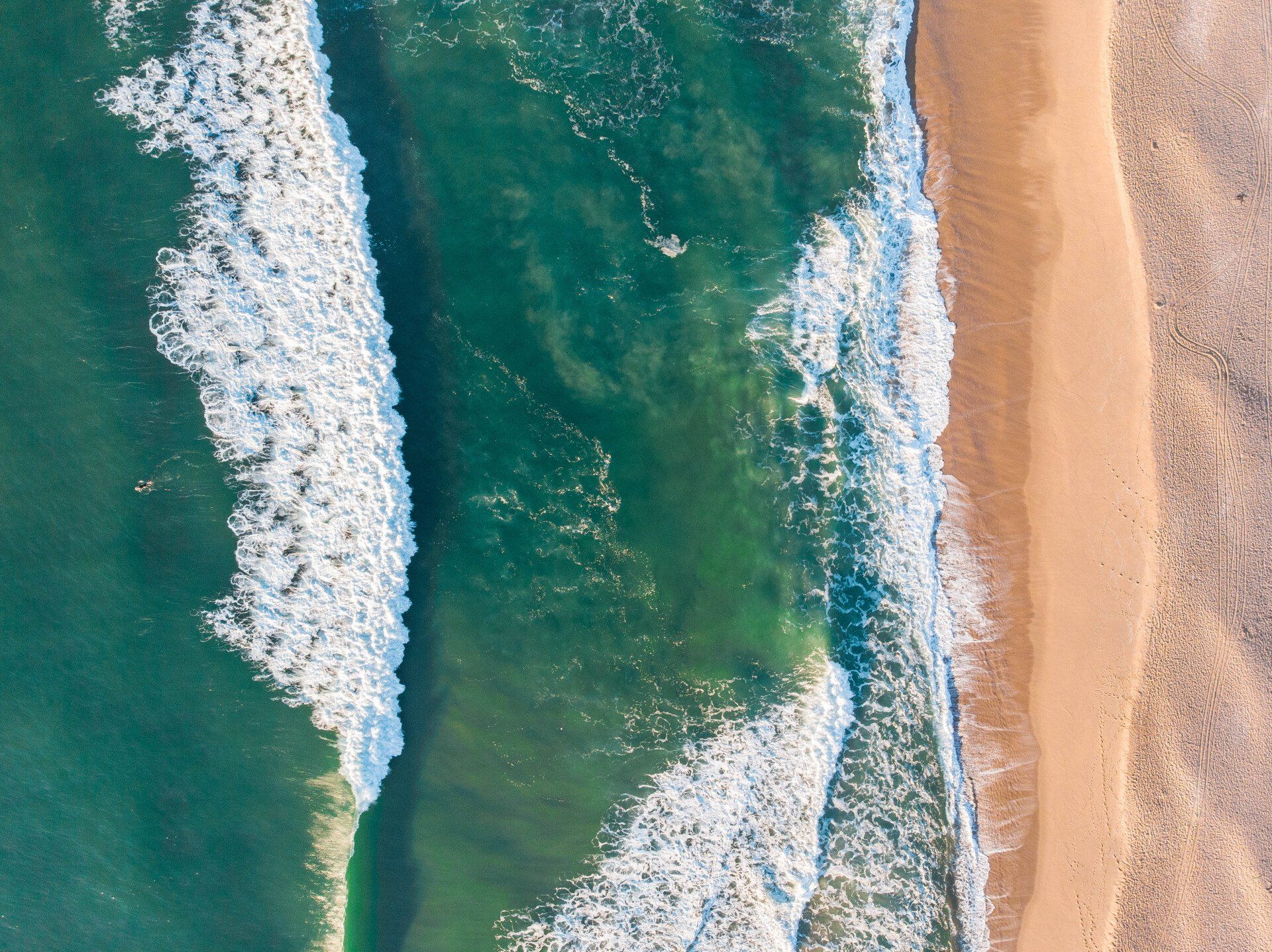 Olas rompiendo en una playa de arena; el agua turquesa se encuentra con la costa color canela.
