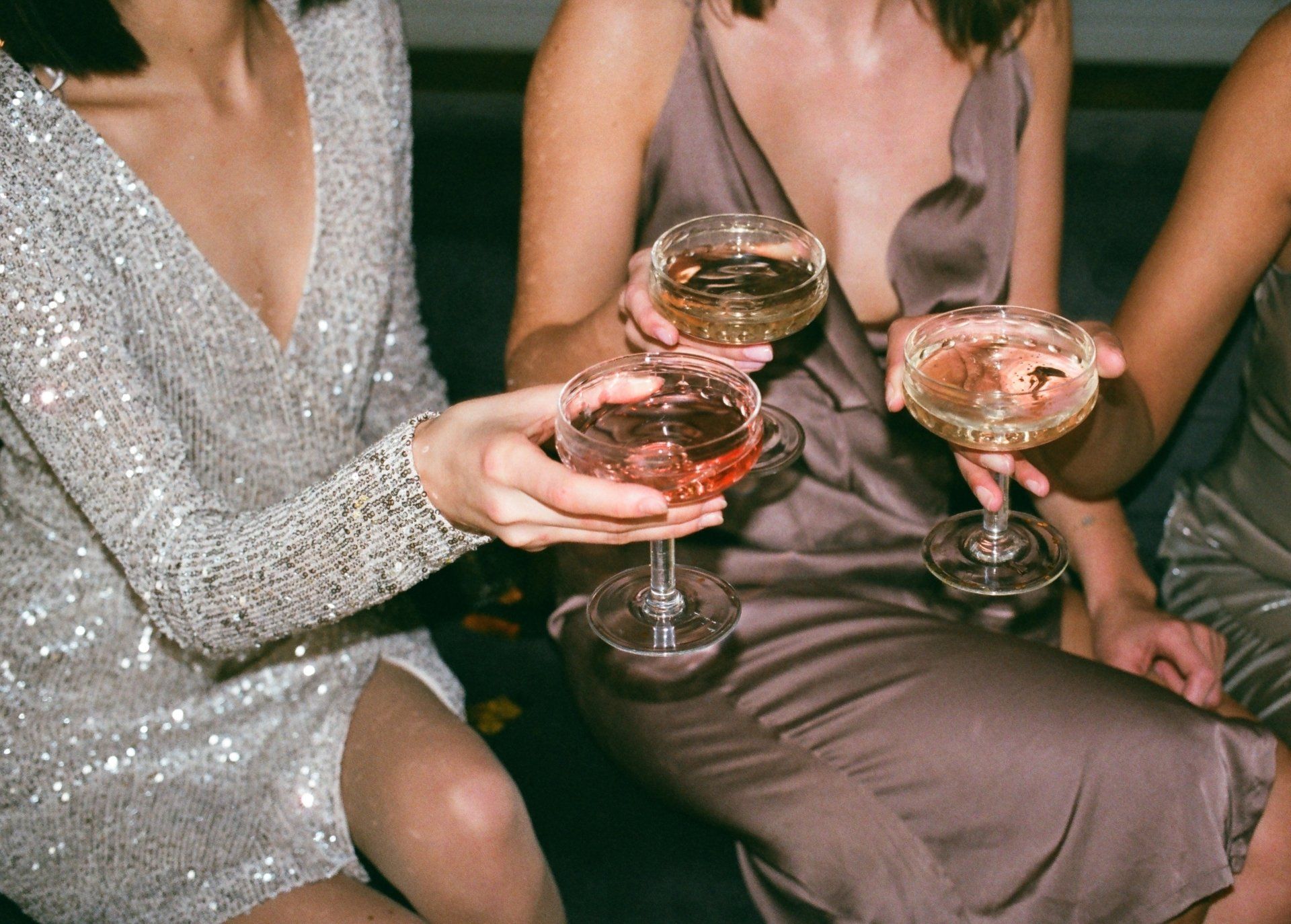 Three women are sitting on a couch holding champagne glasses