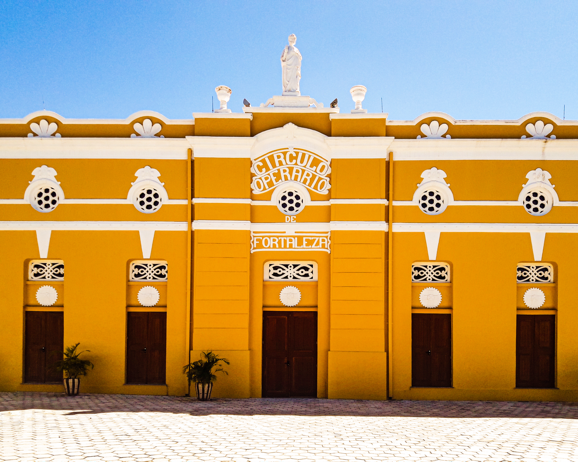 Bright yellow colonial building with white trim, arched windows, and a central ornate doorway under a blue sky