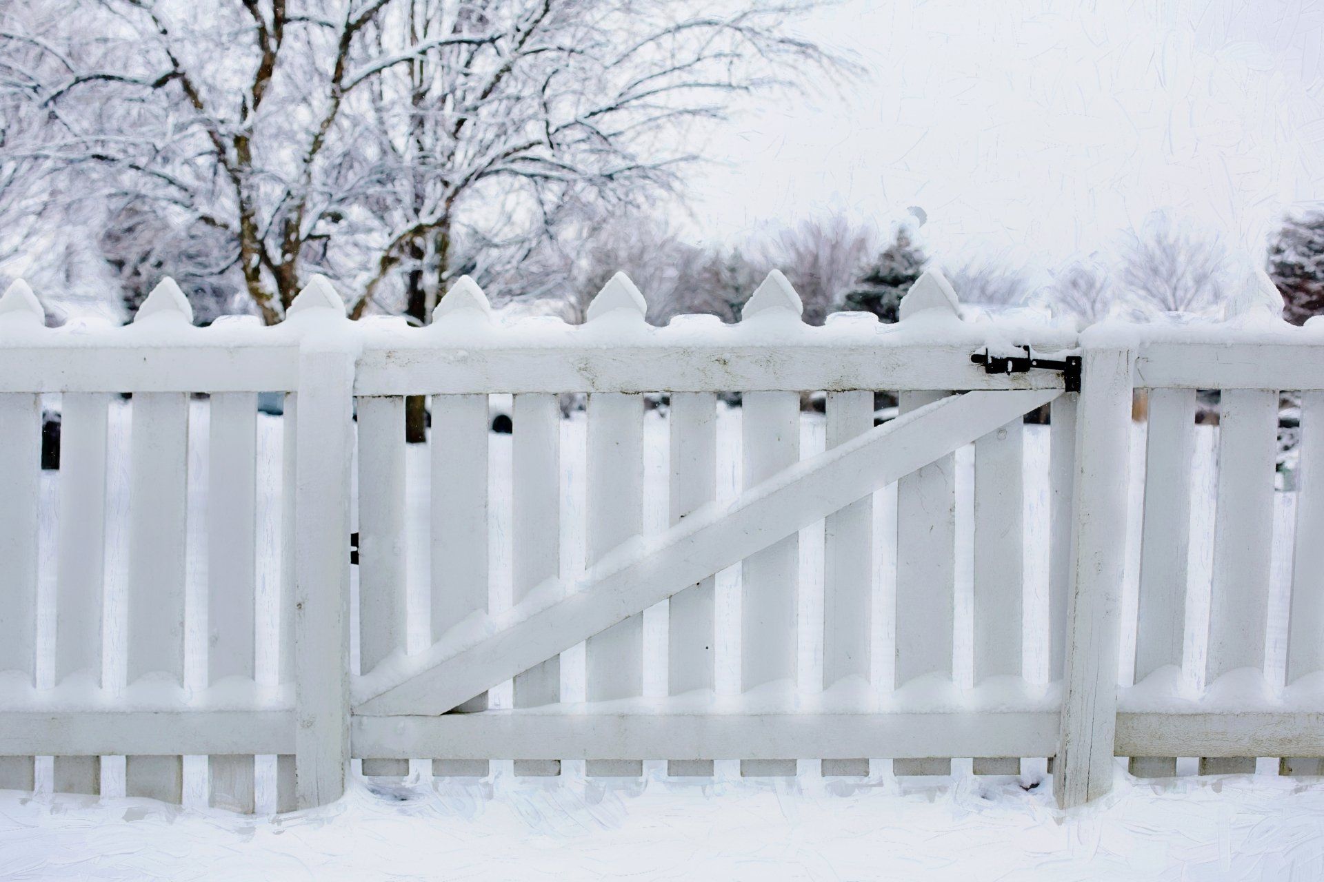 Snow-covered white picket fence and gate in a winter landscape