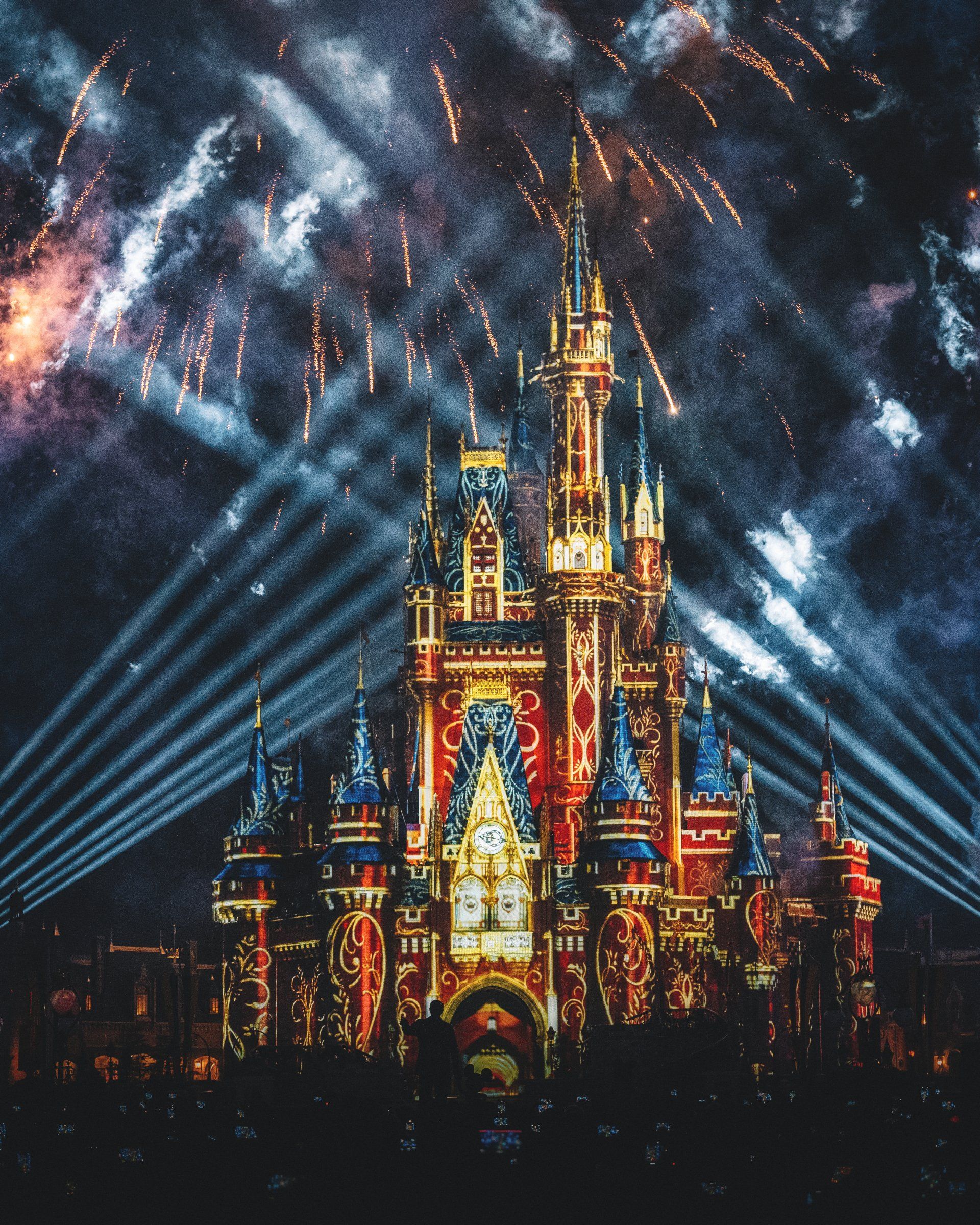 A castle is lit up at night with fireworks in the background