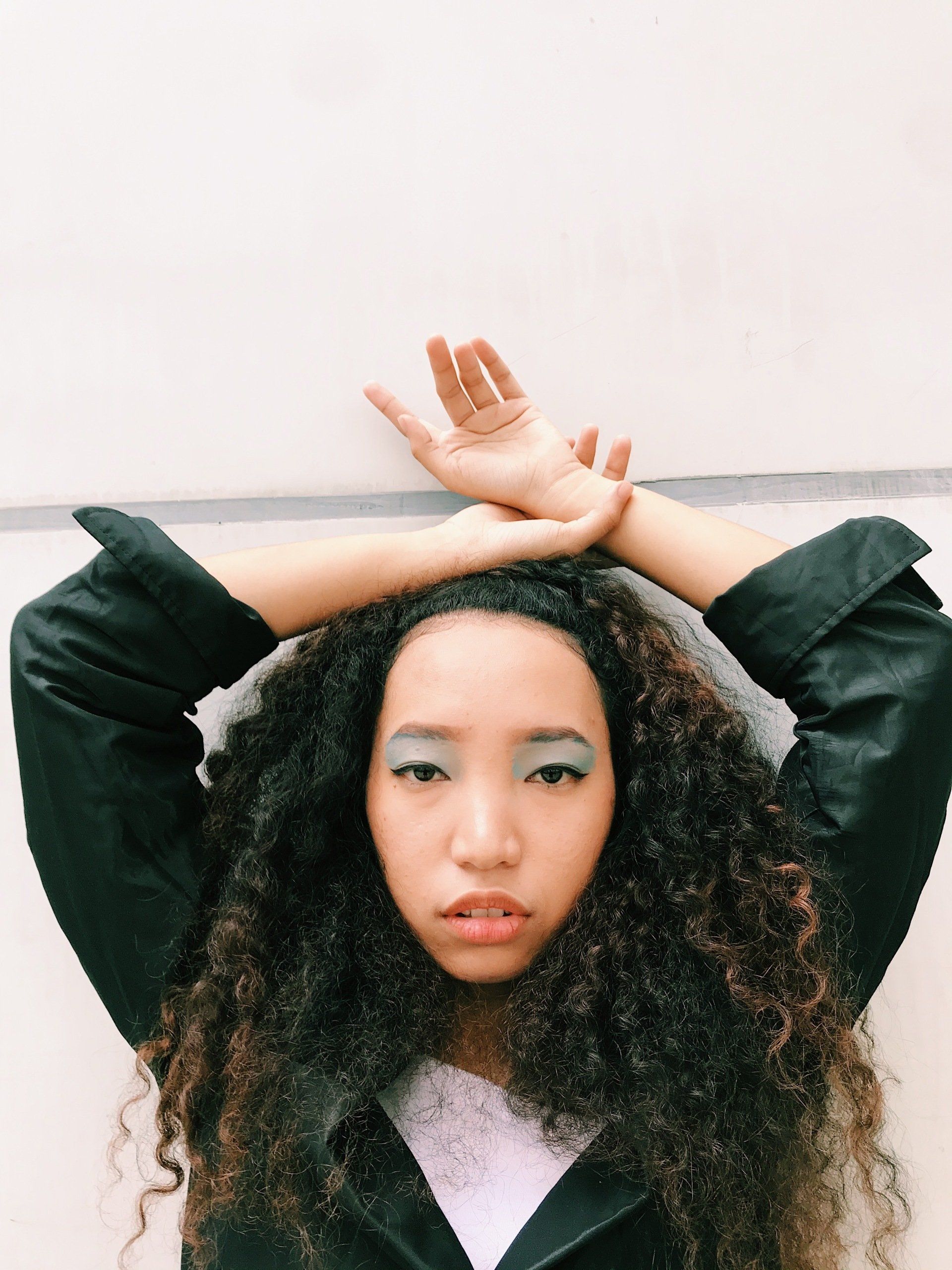 A woman with curly hair is holding her hands over her head