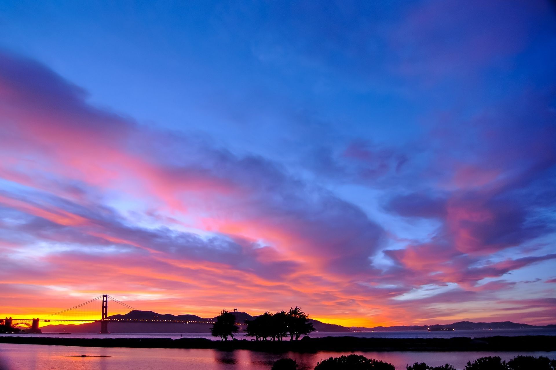 A sunset over a body of water with a bridge in the background.