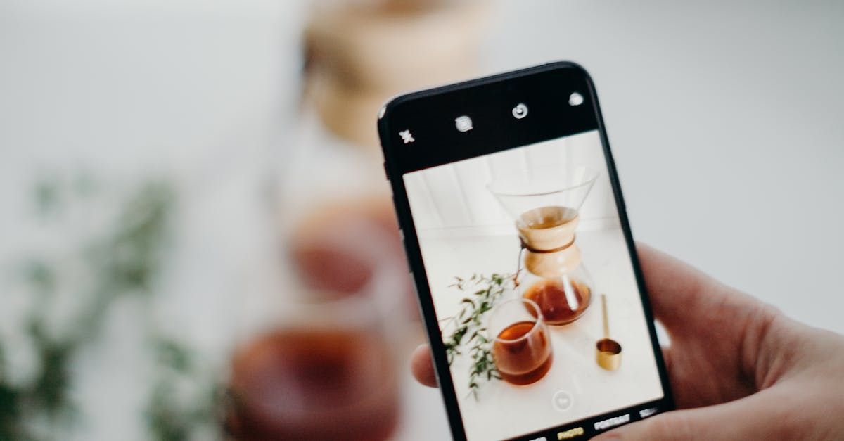A person is holding a cell phone in their hand and taking a picture of a coffee pot.