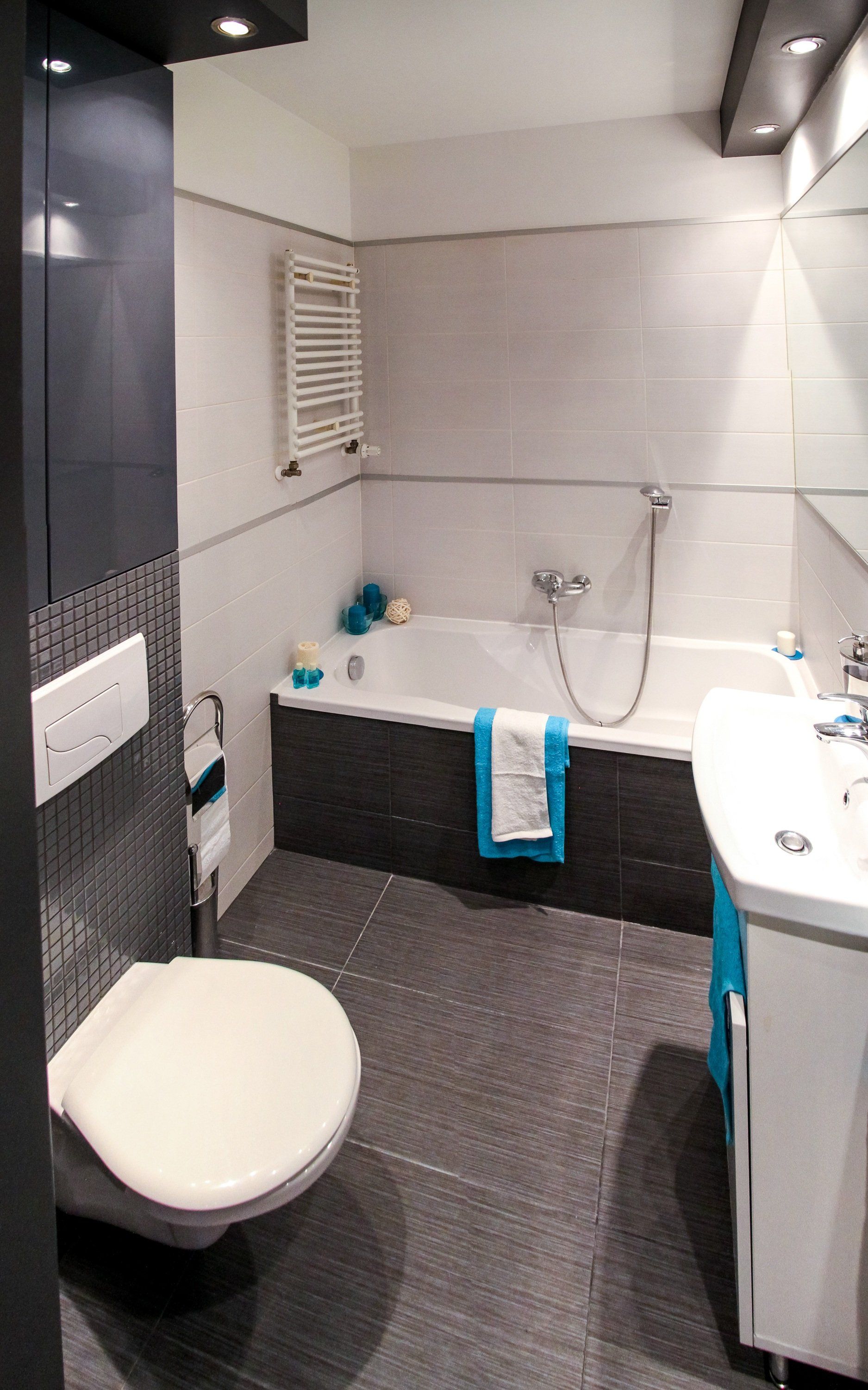 Bathroom with white tub, toilet, and sink; gray tile floor and accents; blue towel.