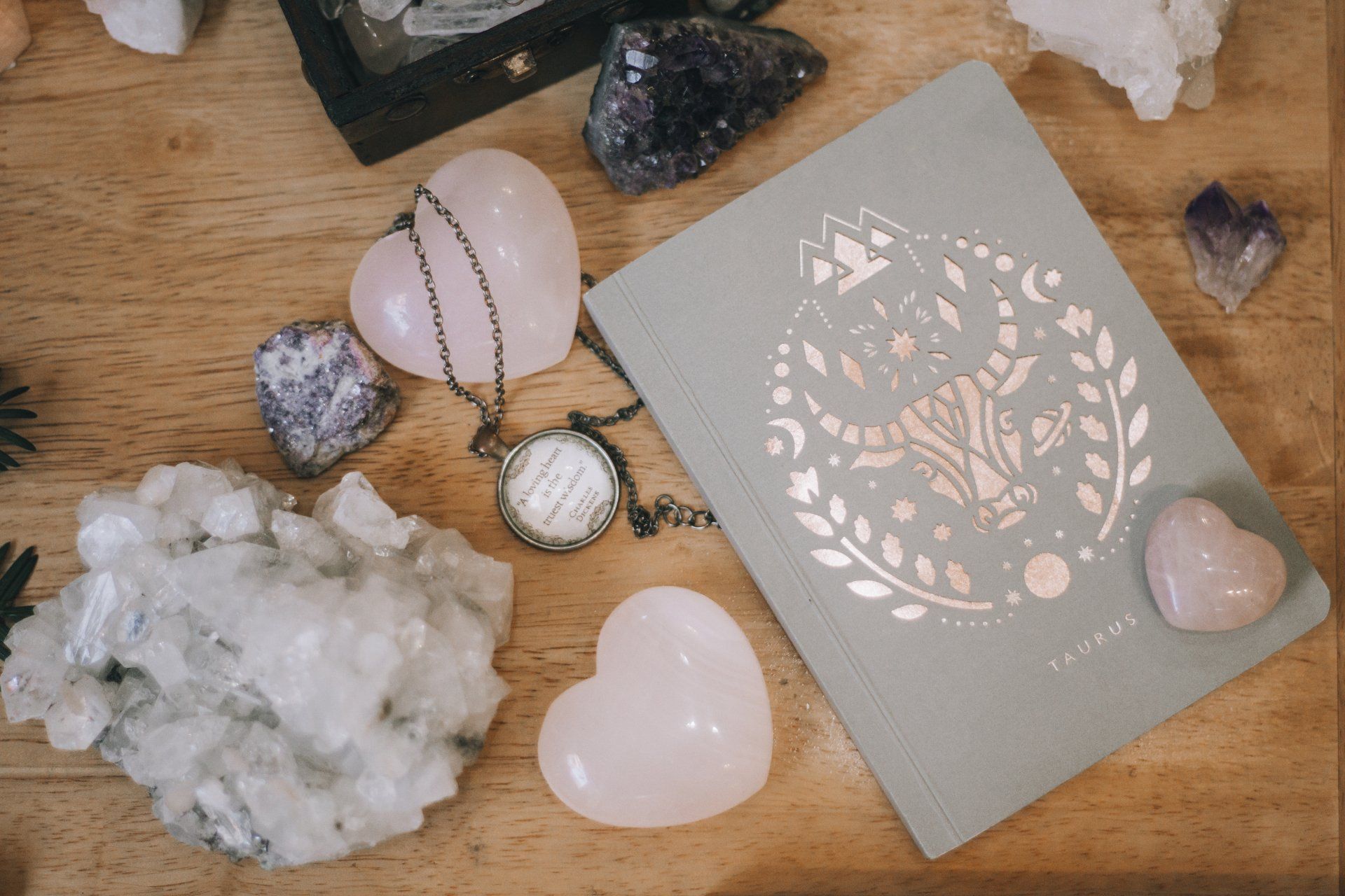 A book surrounded by crystals and a necklace on a wooden table.