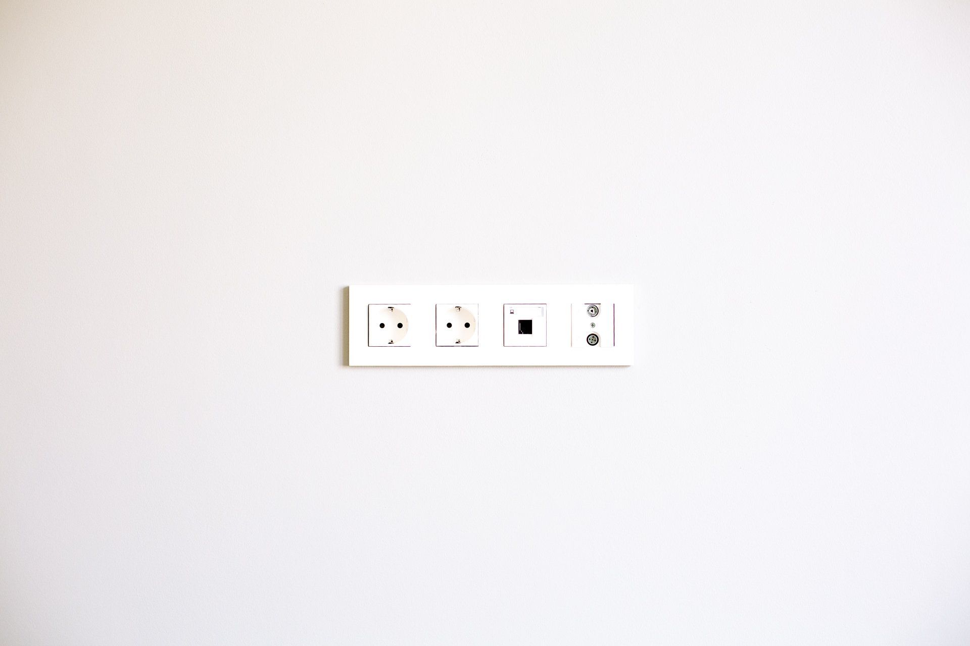 Weiße Wand mit einer rechteckigen Platte mit zwei Steckdosen, einem Datenanschluss und einem Kabelstecker.