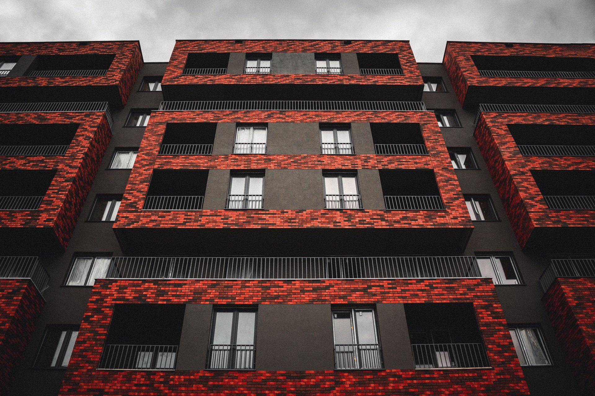 Red brick apartment facade with rows of windows and black balconies viewed from below