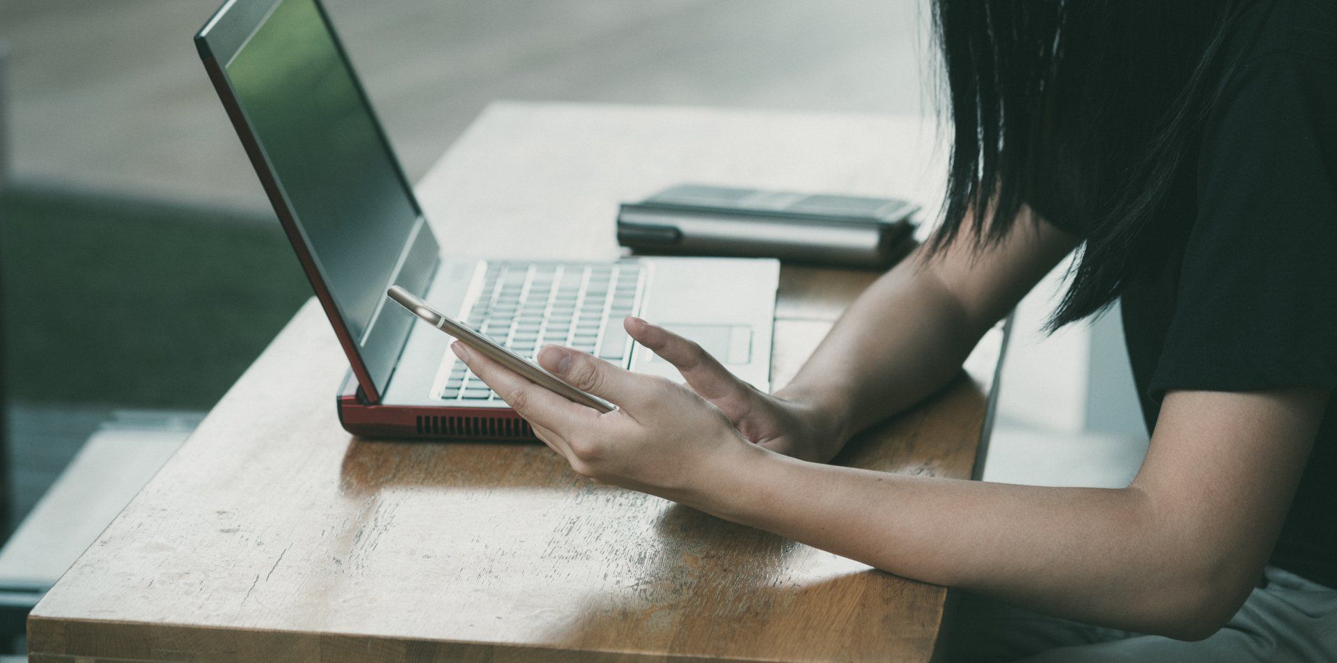 A woman is sitting at a table using a laptop and a cell phone.