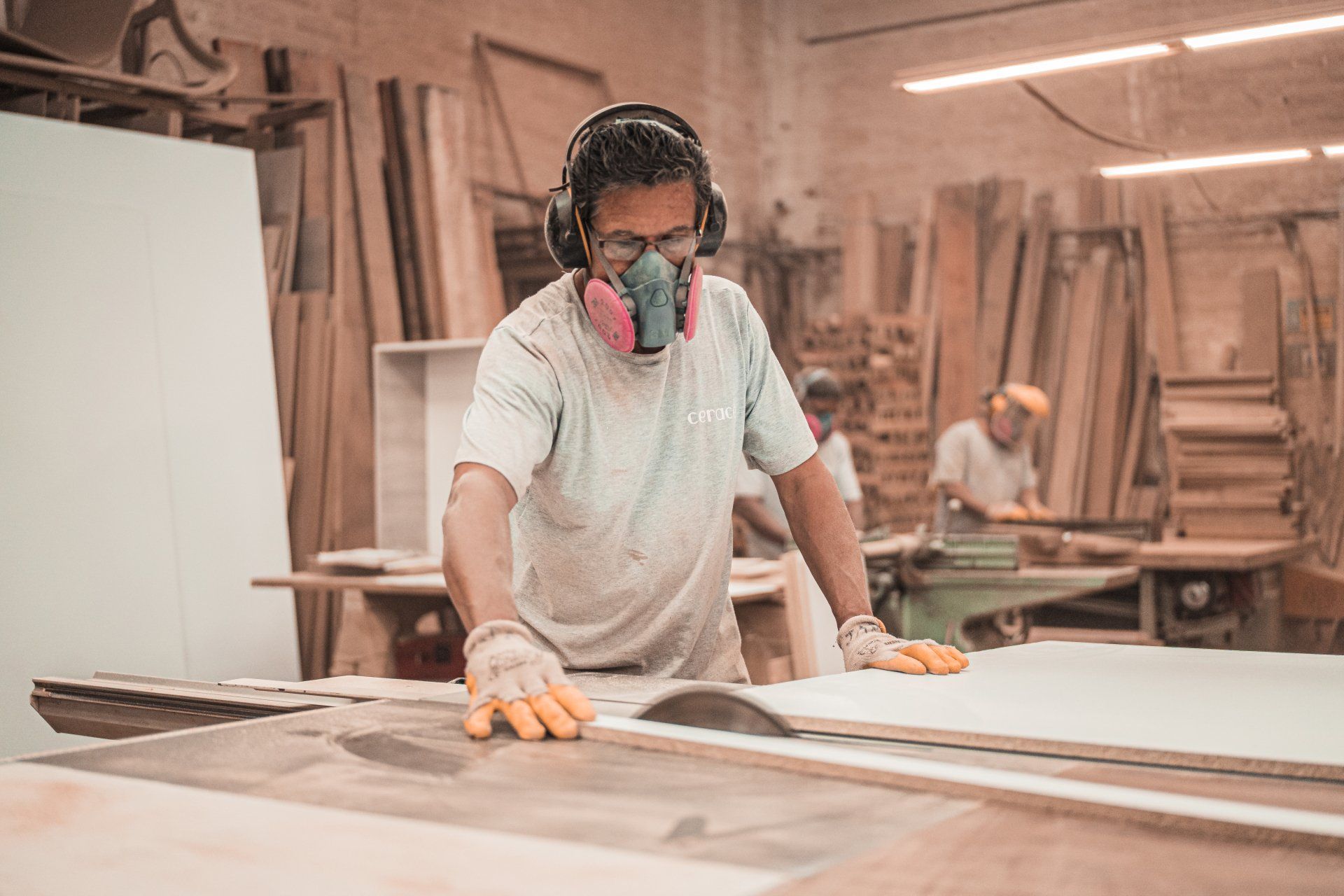 Person wearing safety gear uses a circular saw in a wood workshop.