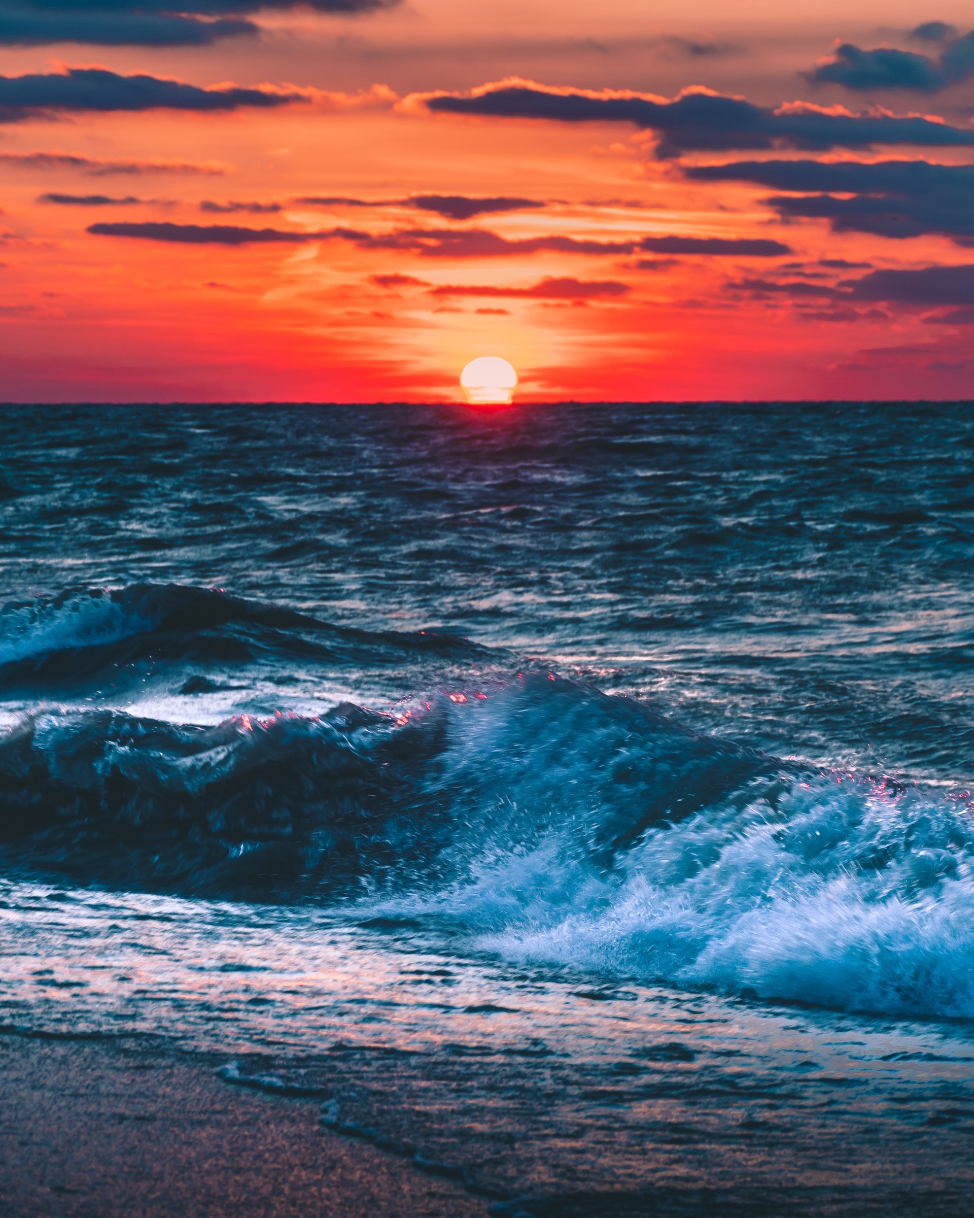 The sun is setting over the ocean and the waves are crashing on the beach.