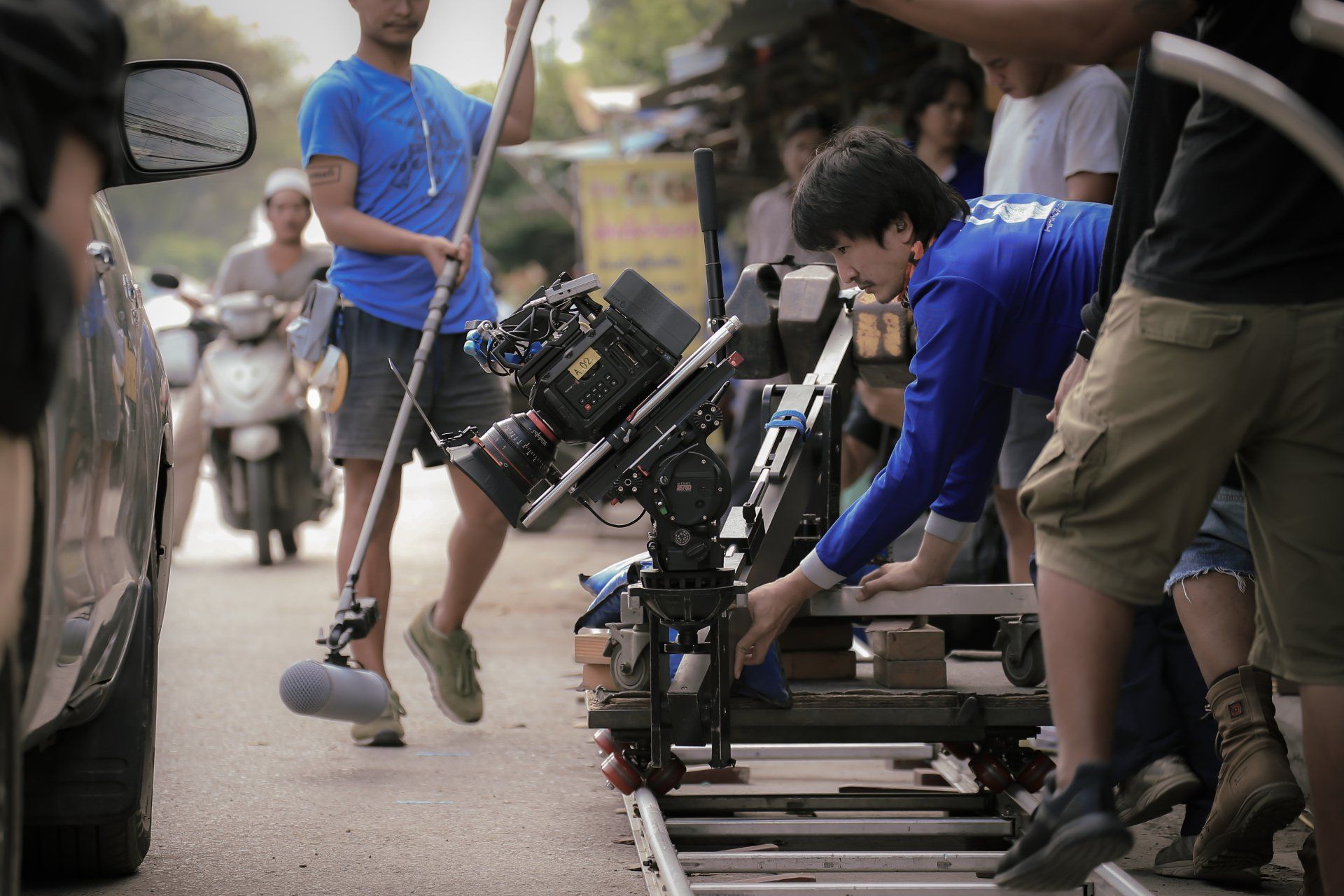 Film crew using a camera on dolly tracks on a busy street, with a sound recordist holding a boom mic nearby.