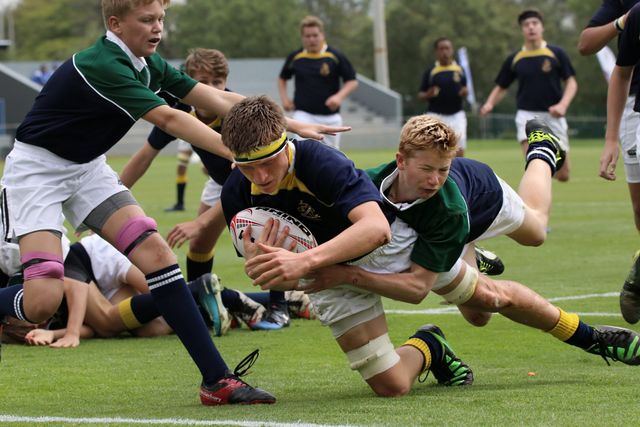 Des joueurs de rugby plaquent un coureur sur un terrain herbeux pendant un match.