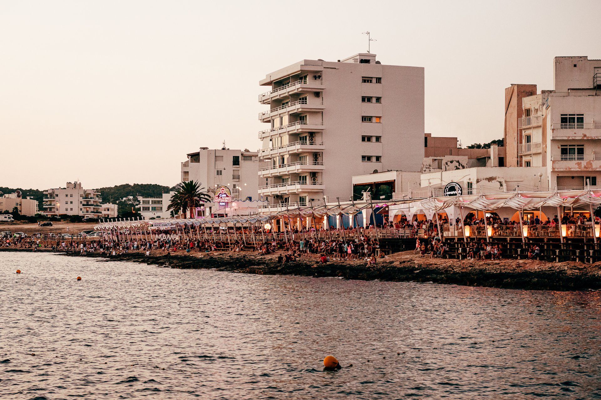 Coastal buildings and a crowd of people gathered near the water during the day.
