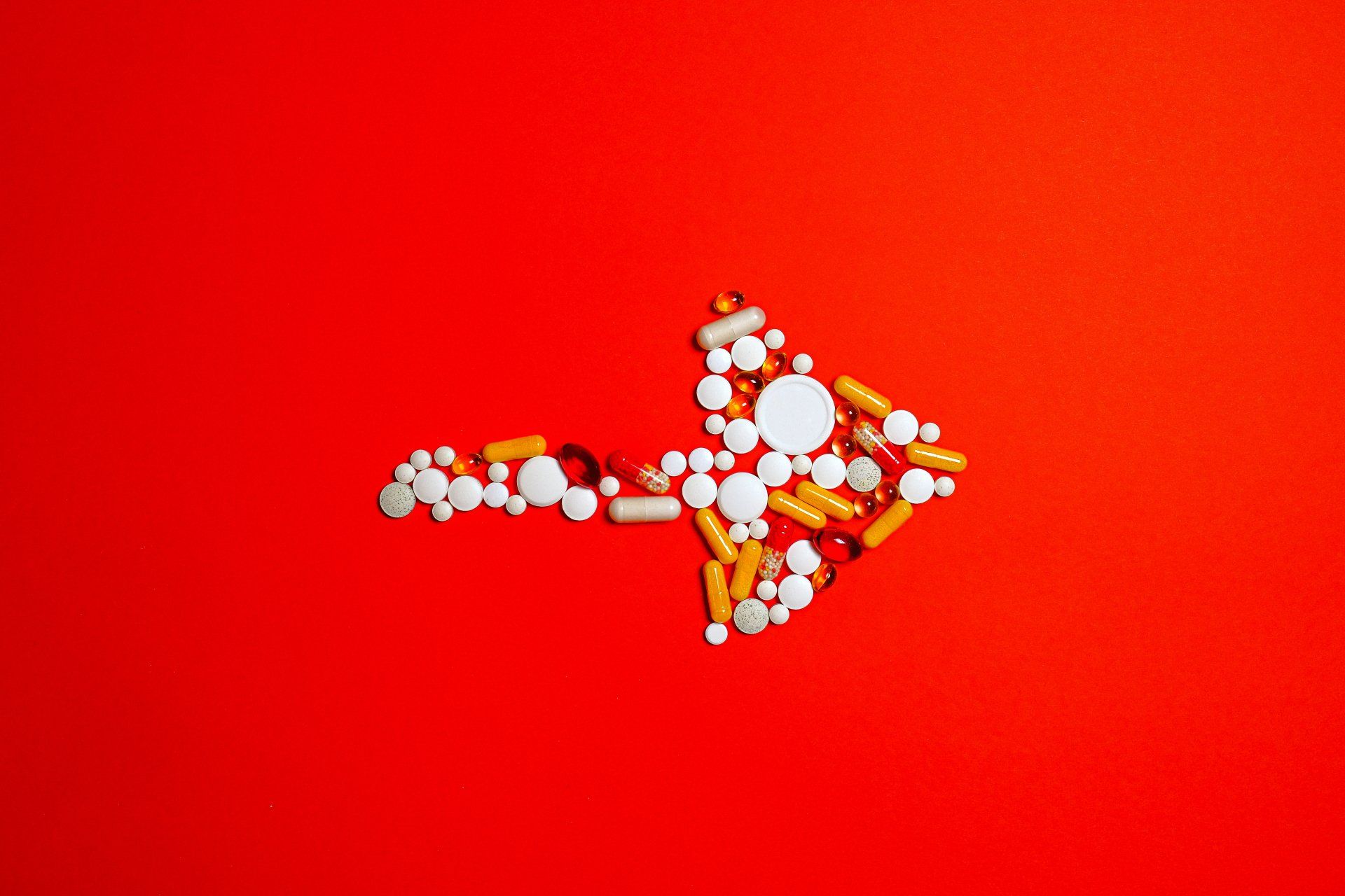 Arrow made of white and orange pills on a red background