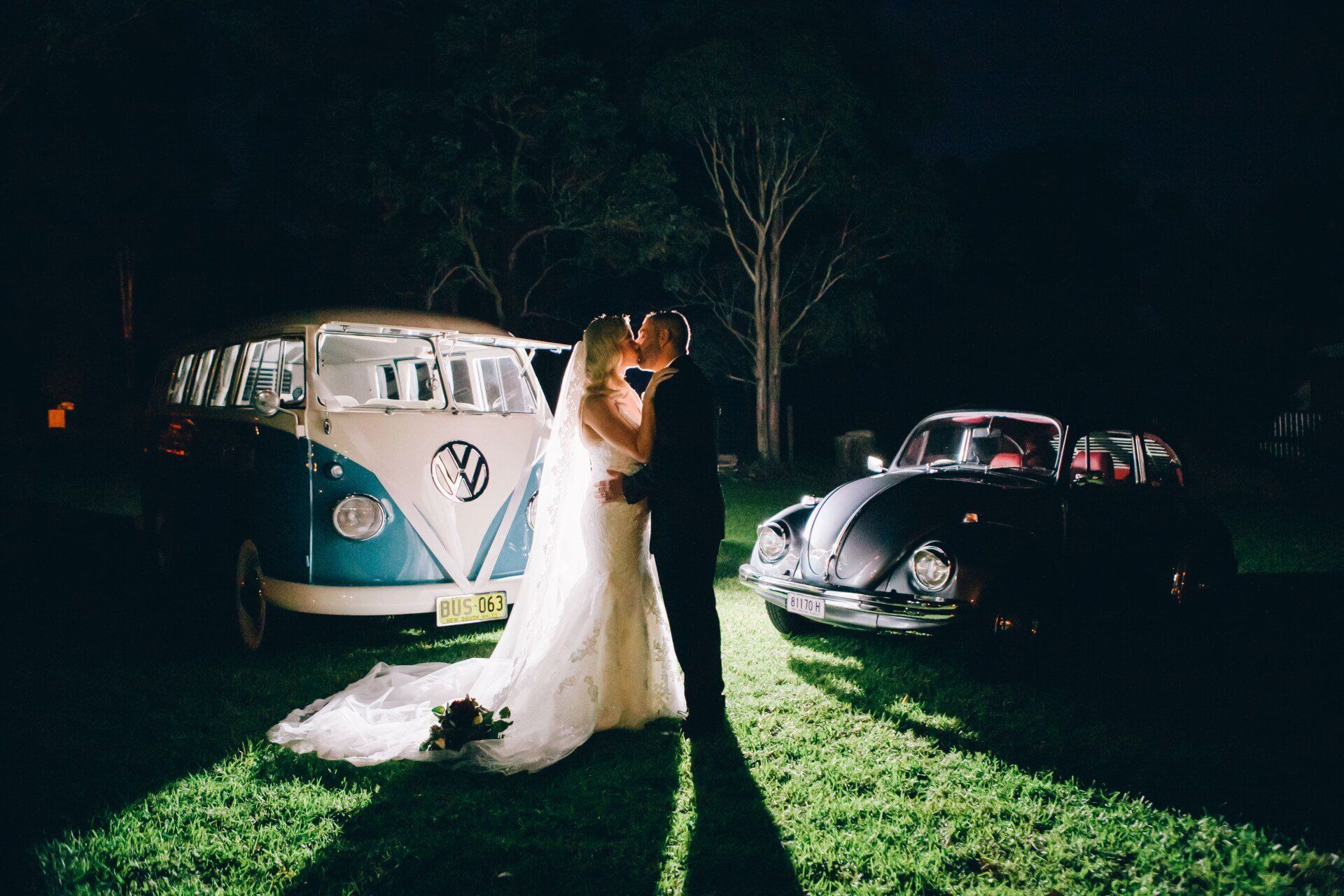 Bride and groom standing between a white VW van and black car at night outdoors