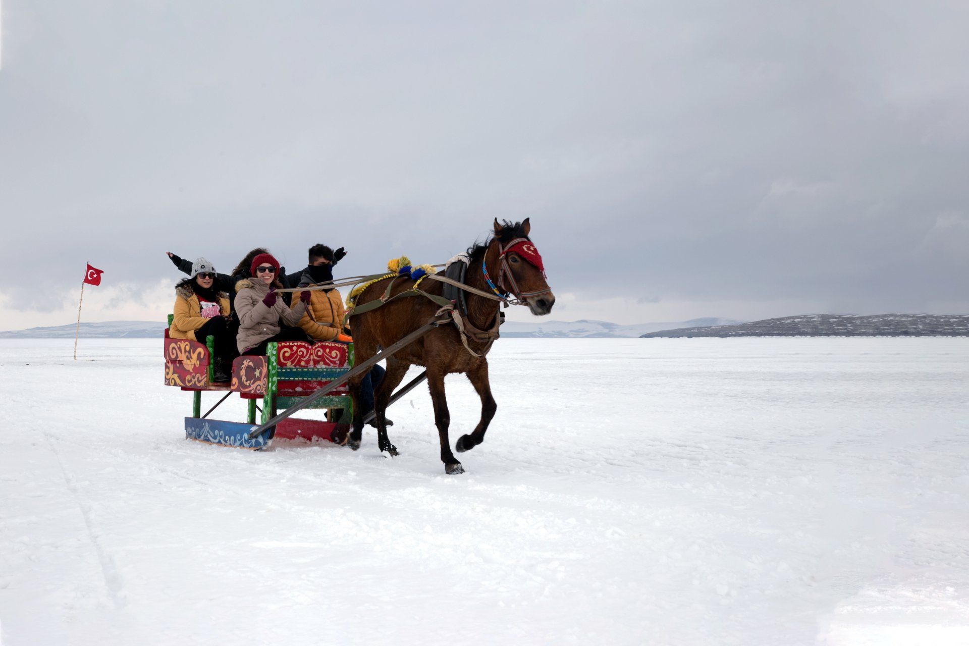 Ein von Pferden gezogener Schlitten transportiert dick eingepackte Reiter über eine verschneite, gefrorene Landschaft.