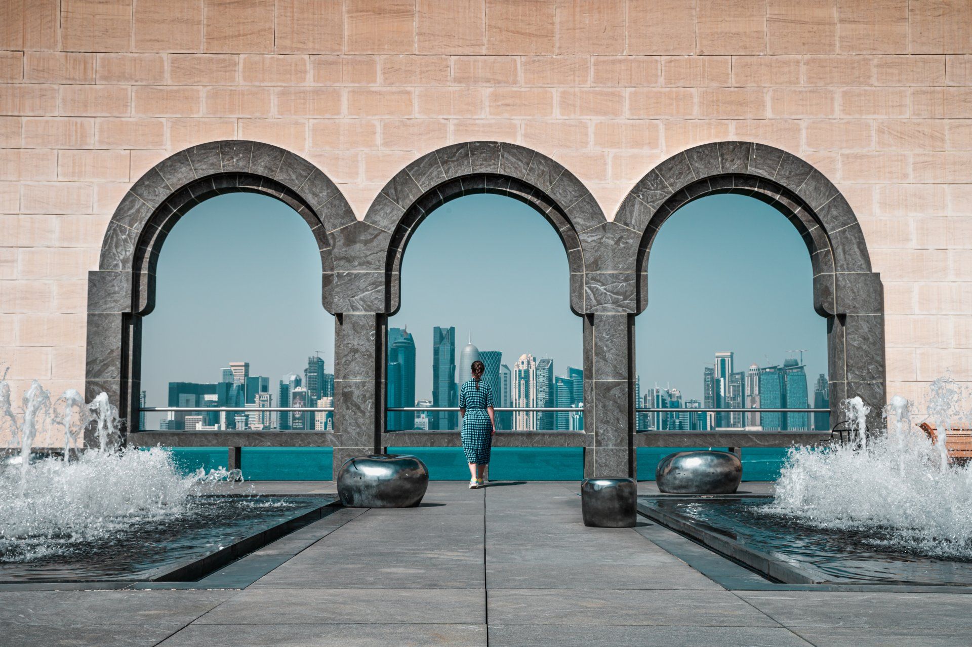 A woman is standing in front of a building with arched windows looking out to a city skyline.