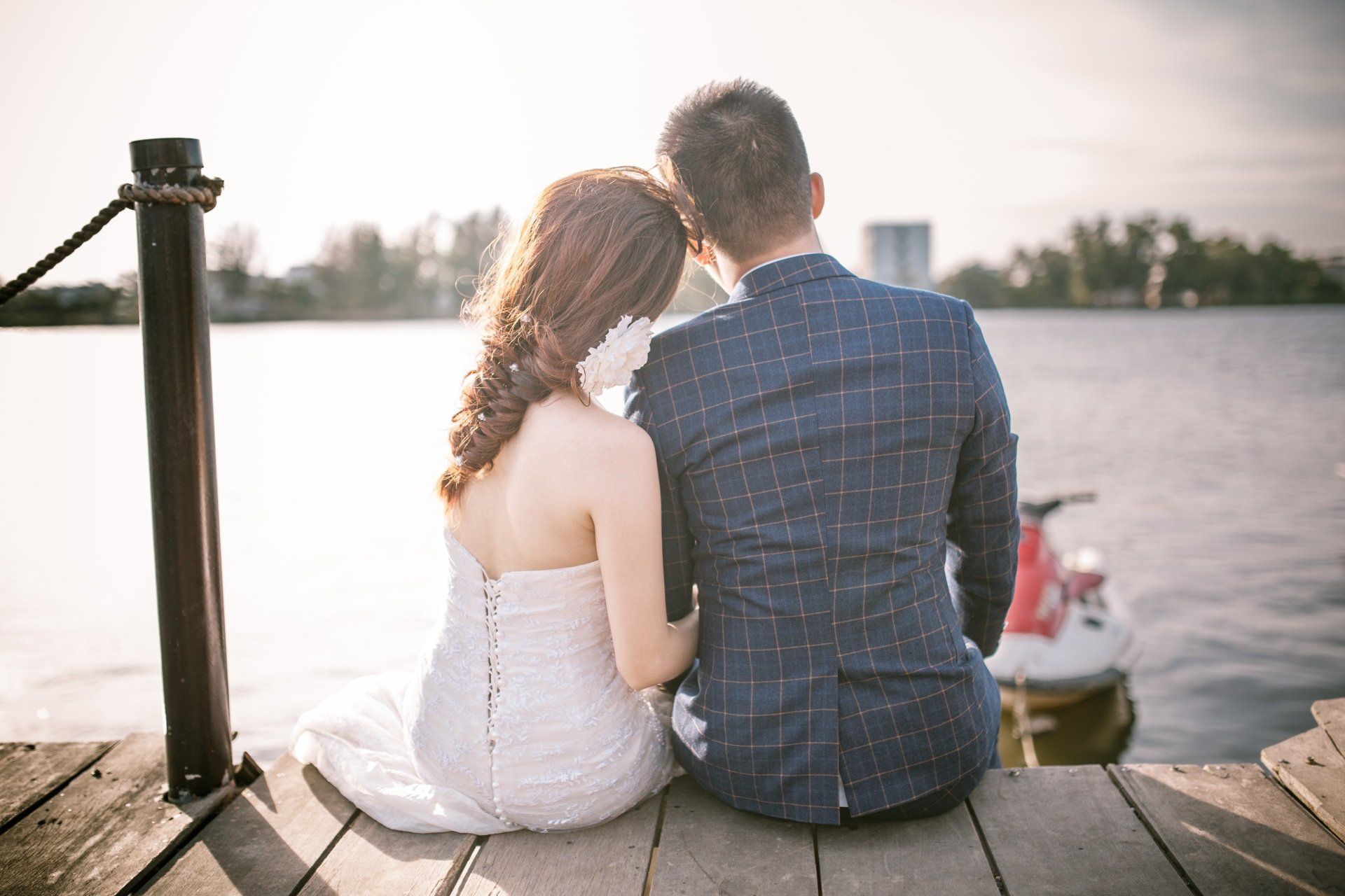 A bride and groom are sitting on a dock looking at the water.