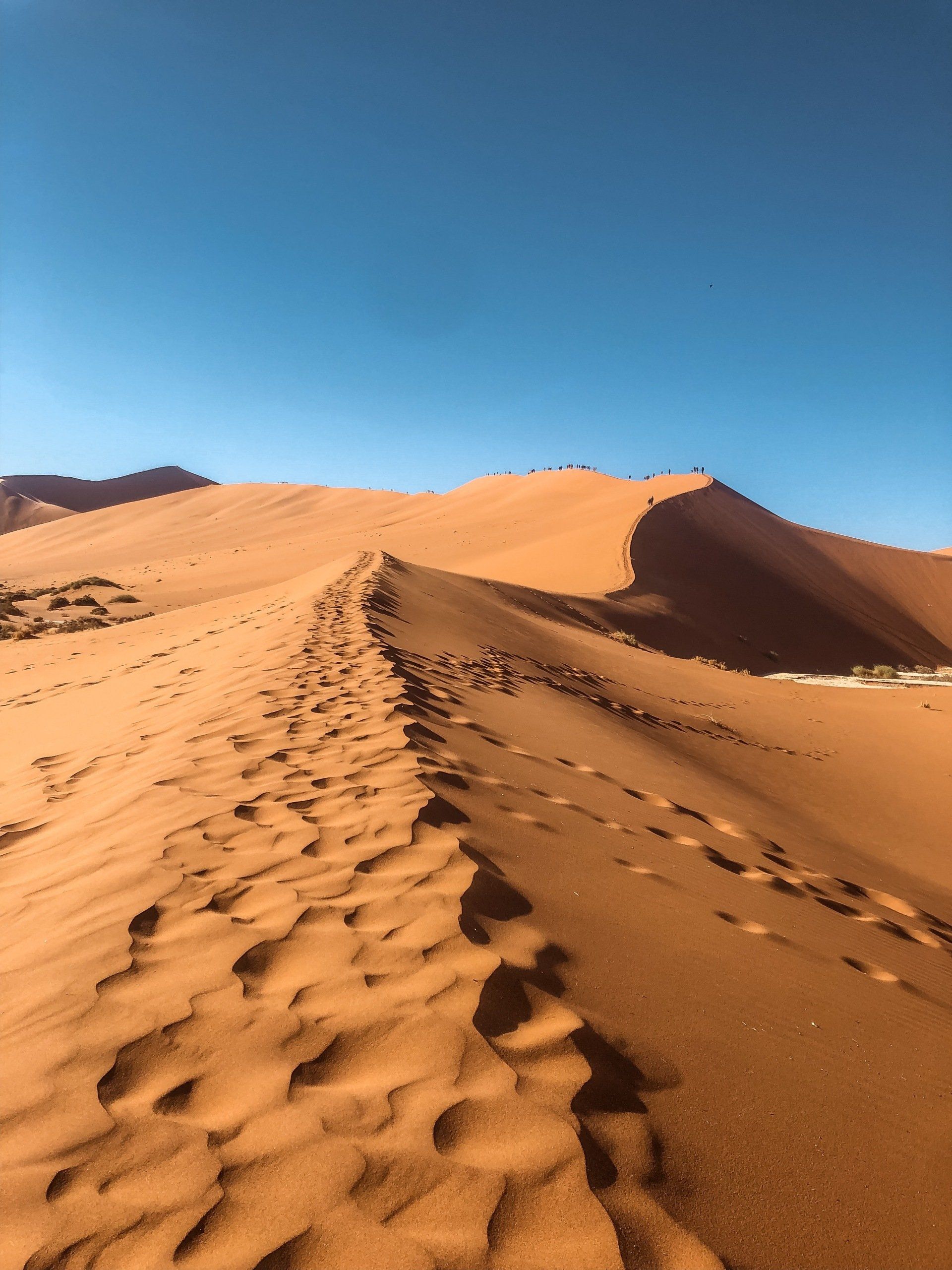 A person is walking up a sand dune in the desert.