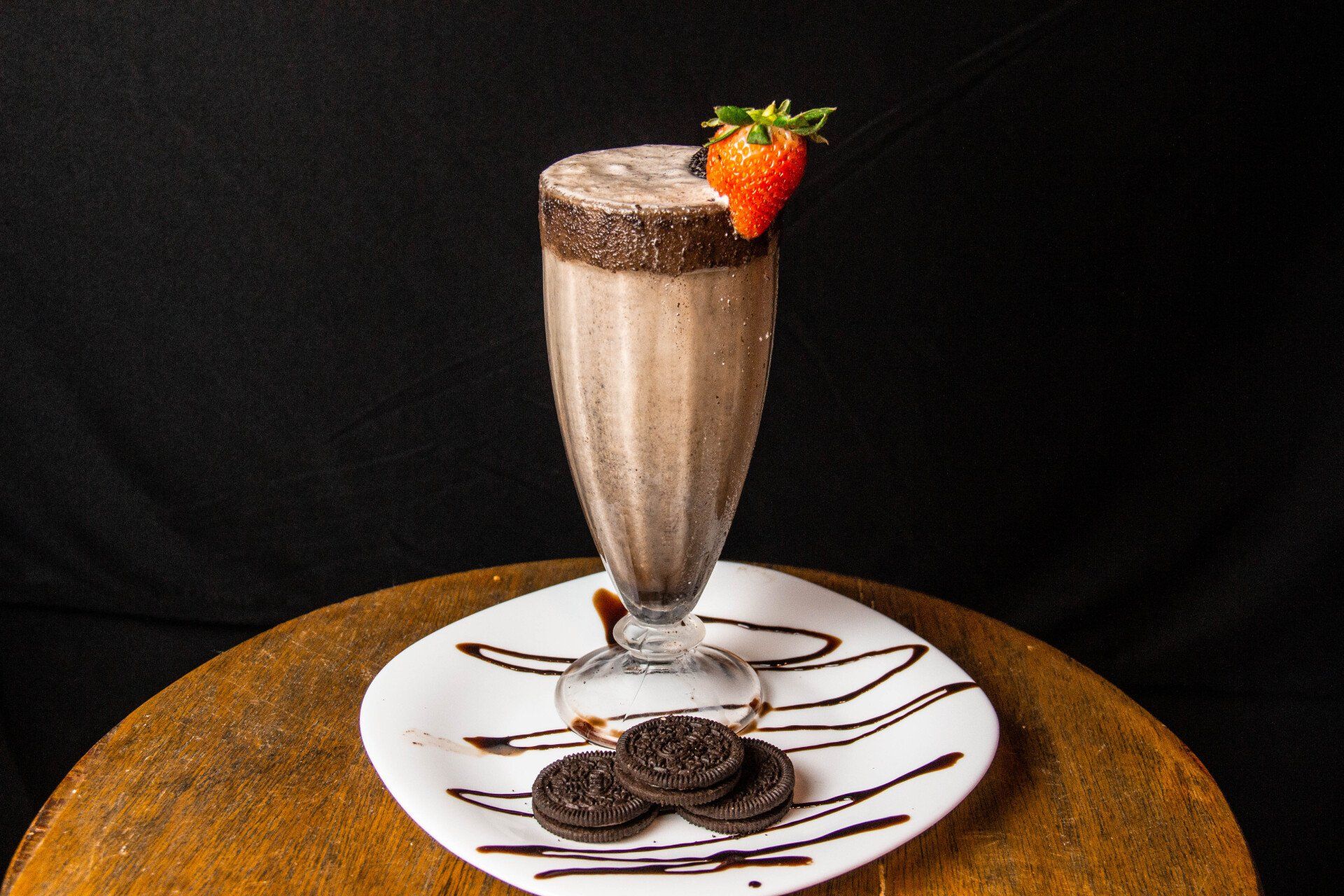 a milkshake with a strawberry on top is on a plate on a table .