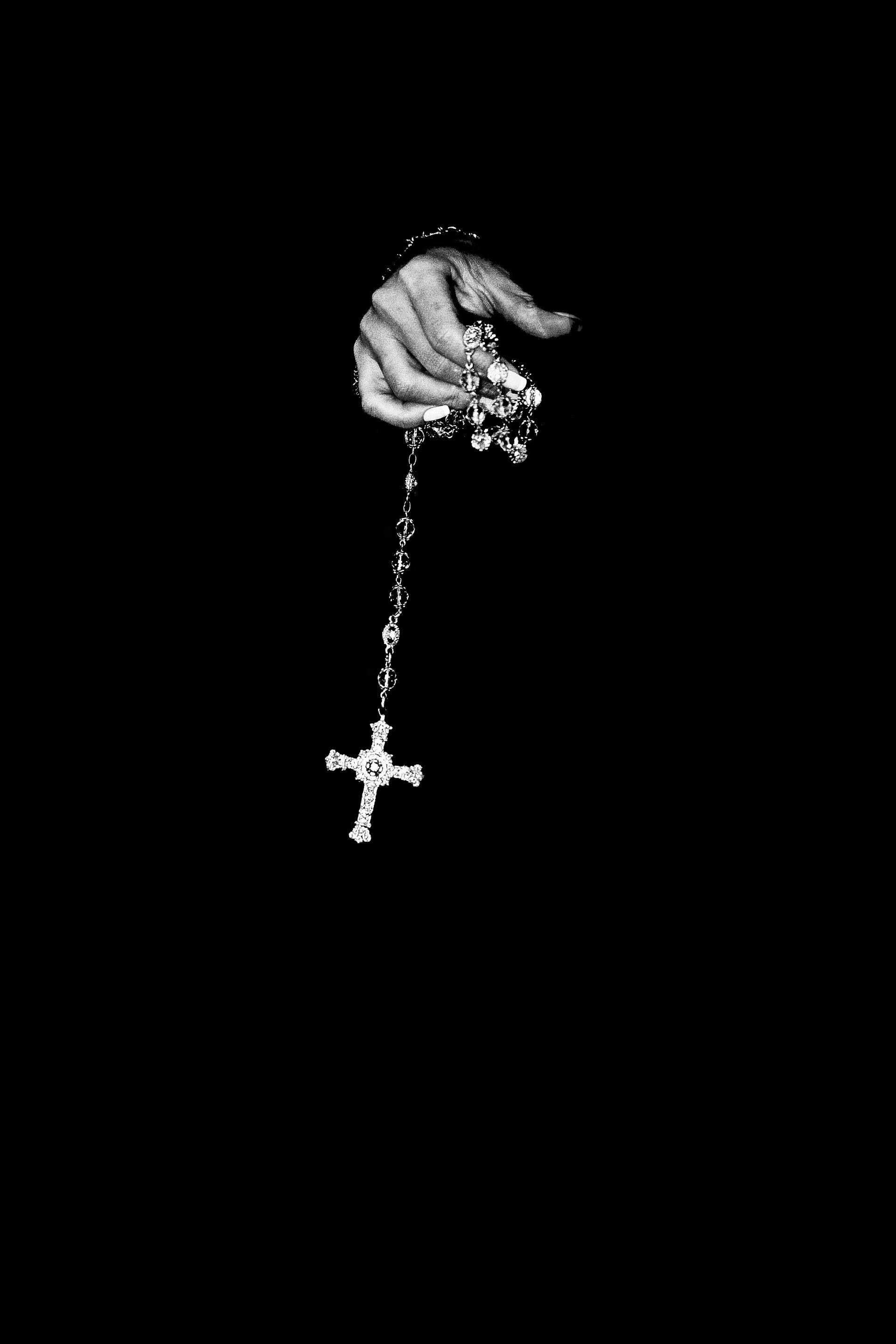 A hand is holding a rosary with a cross on it.