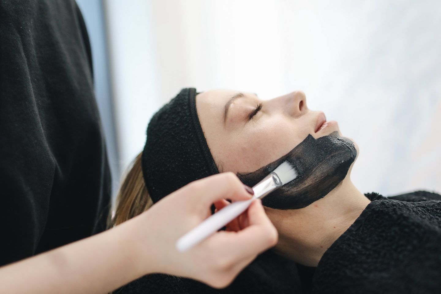 A woman is getting a black mask on her face.