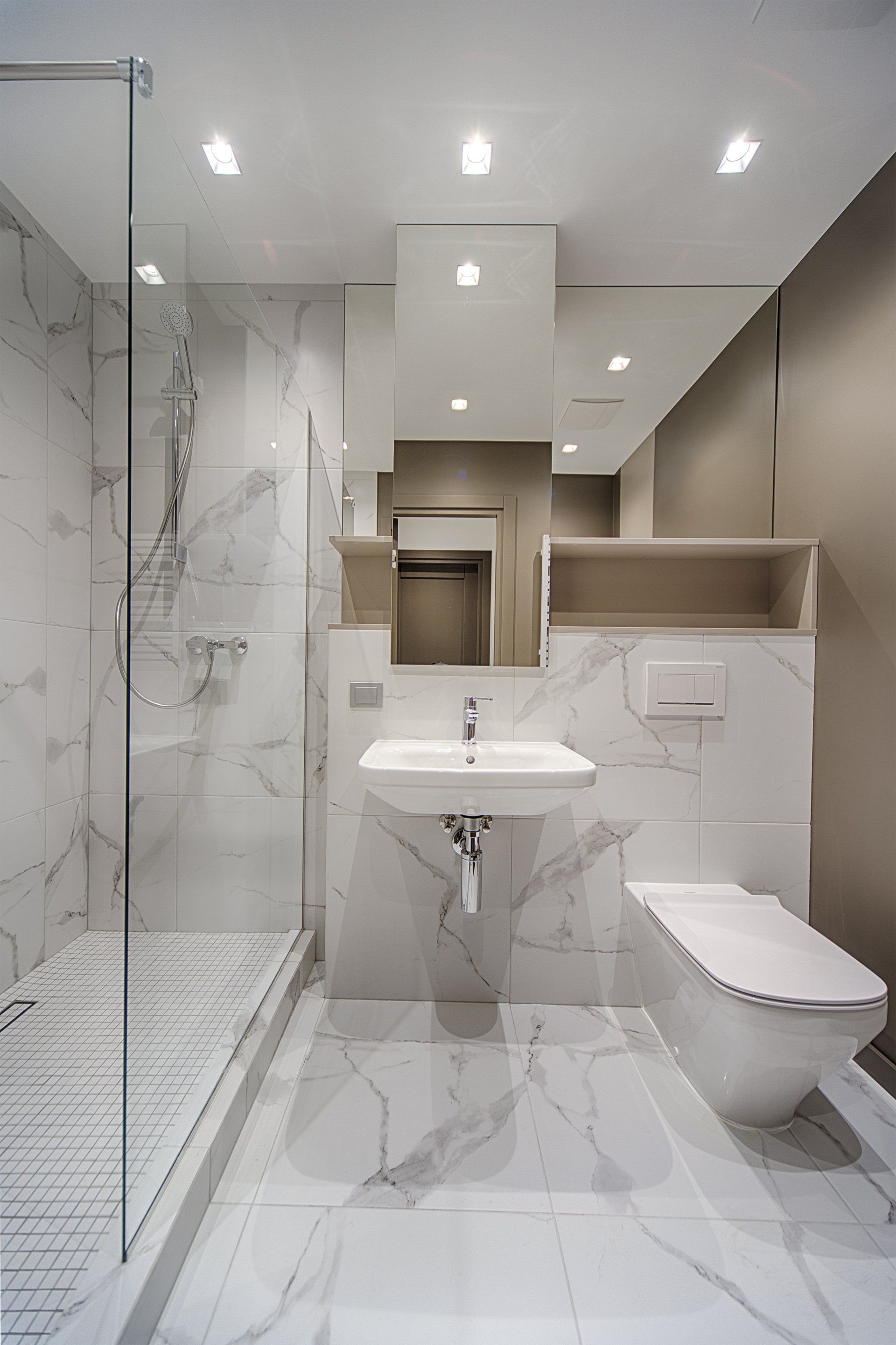 Minimal, modern bathroom with marbled walls throughout the room and shower along with white tiled shower flooring.