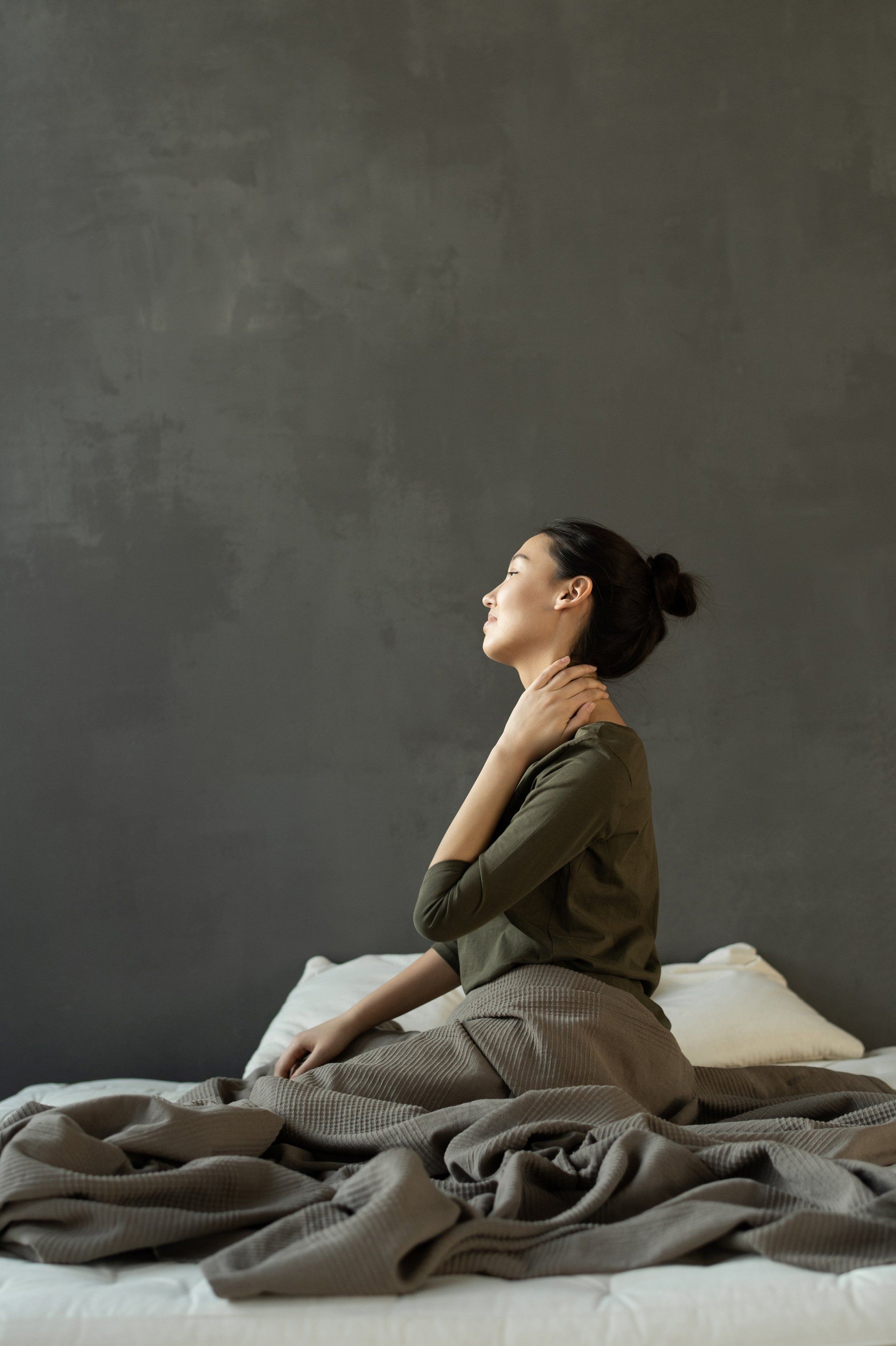 a woman sits on a bed with neck pain