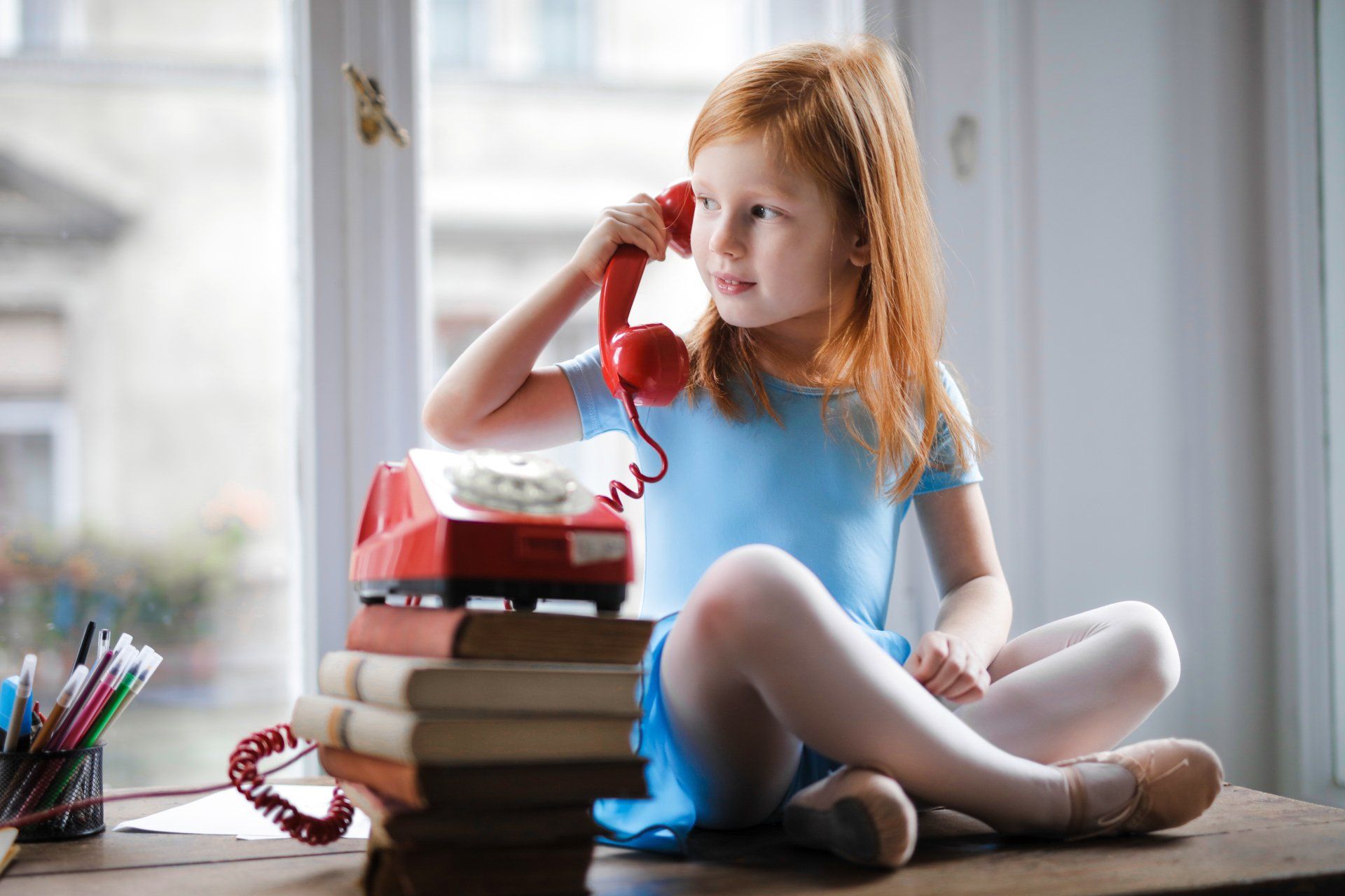 Girl on rotary dial phone looking out a window
