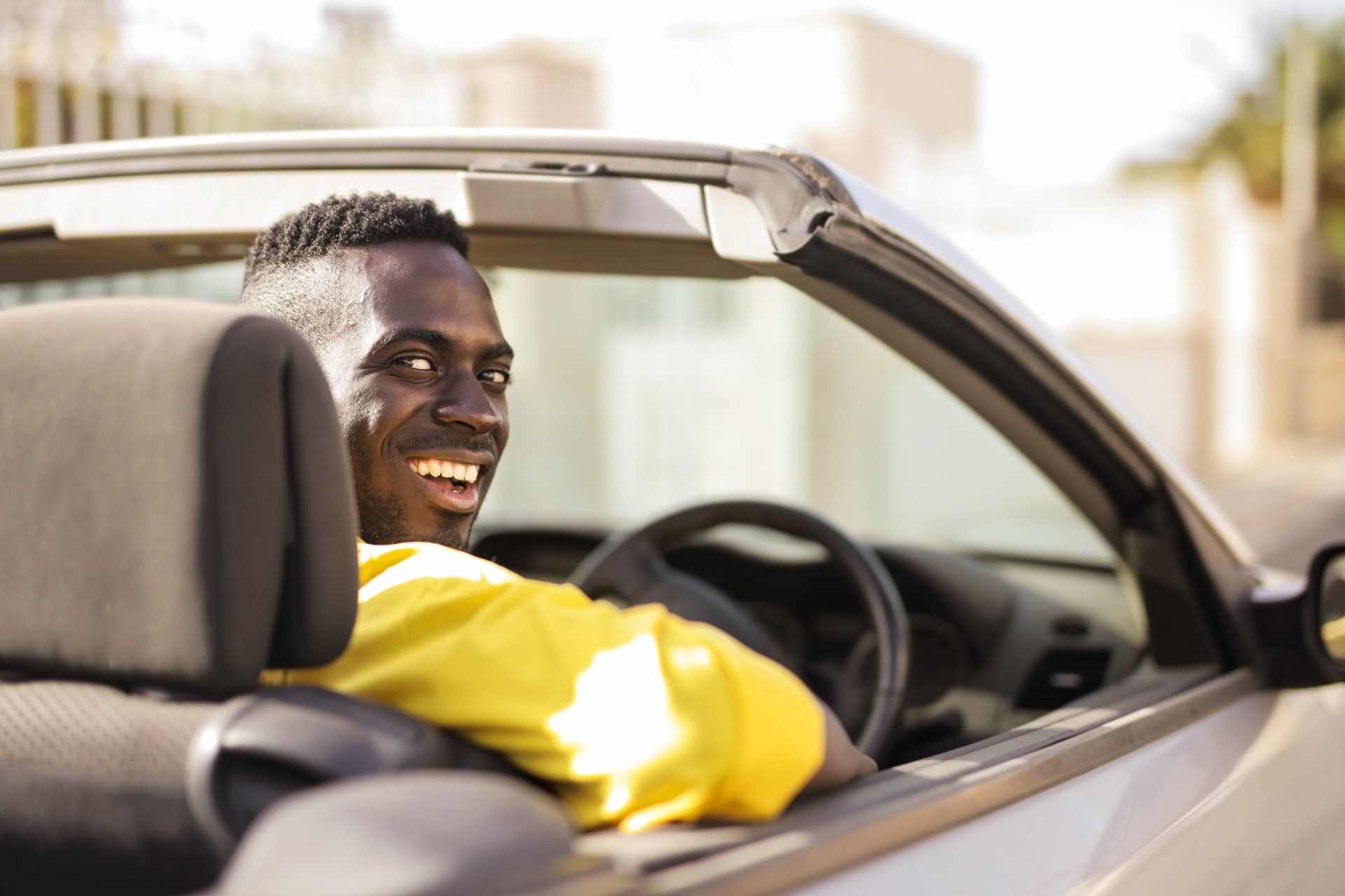 A man is sitting in a convertible car and smiling.