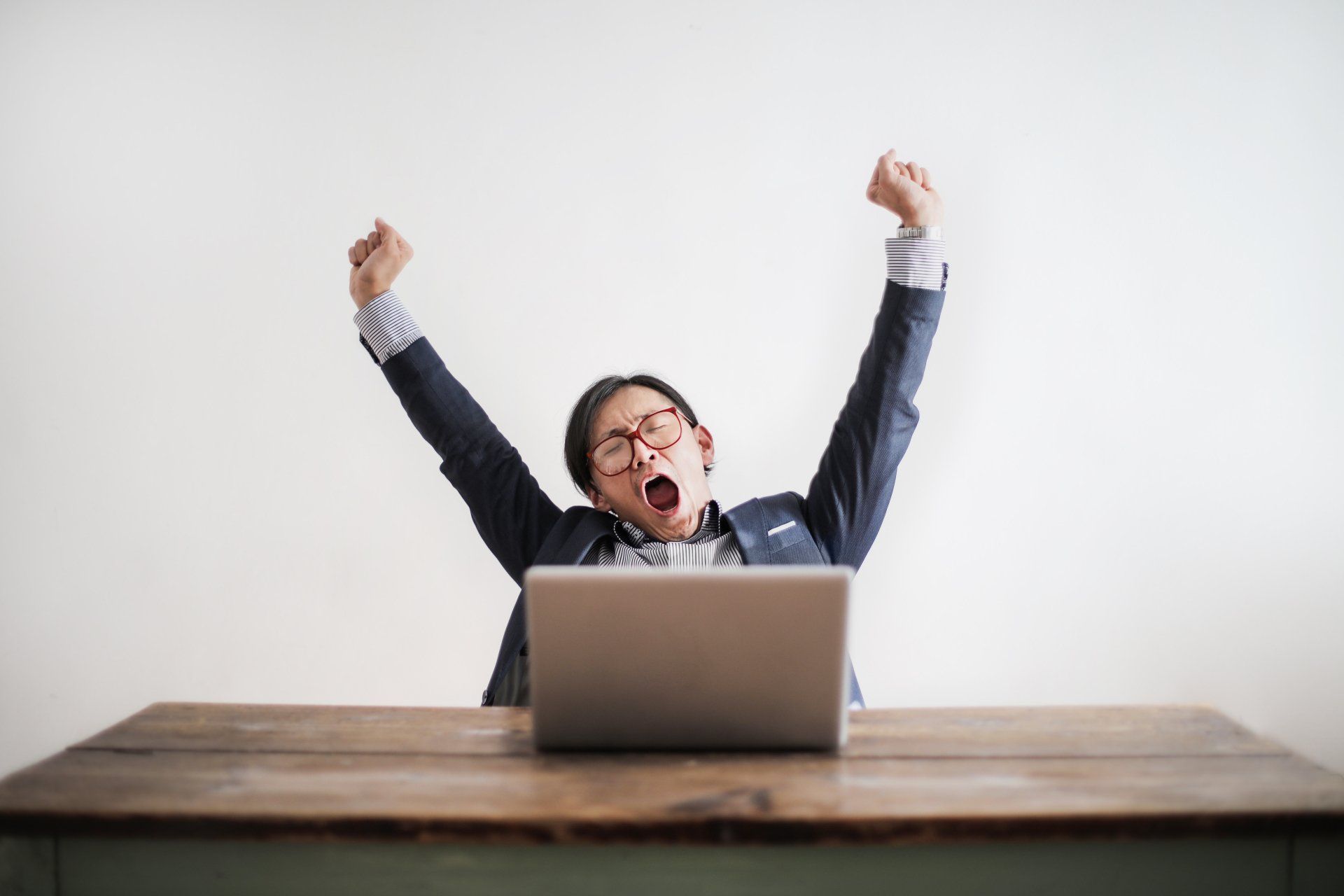 a man is sitting at a desk with his arms in the air in front of a laptop computer .