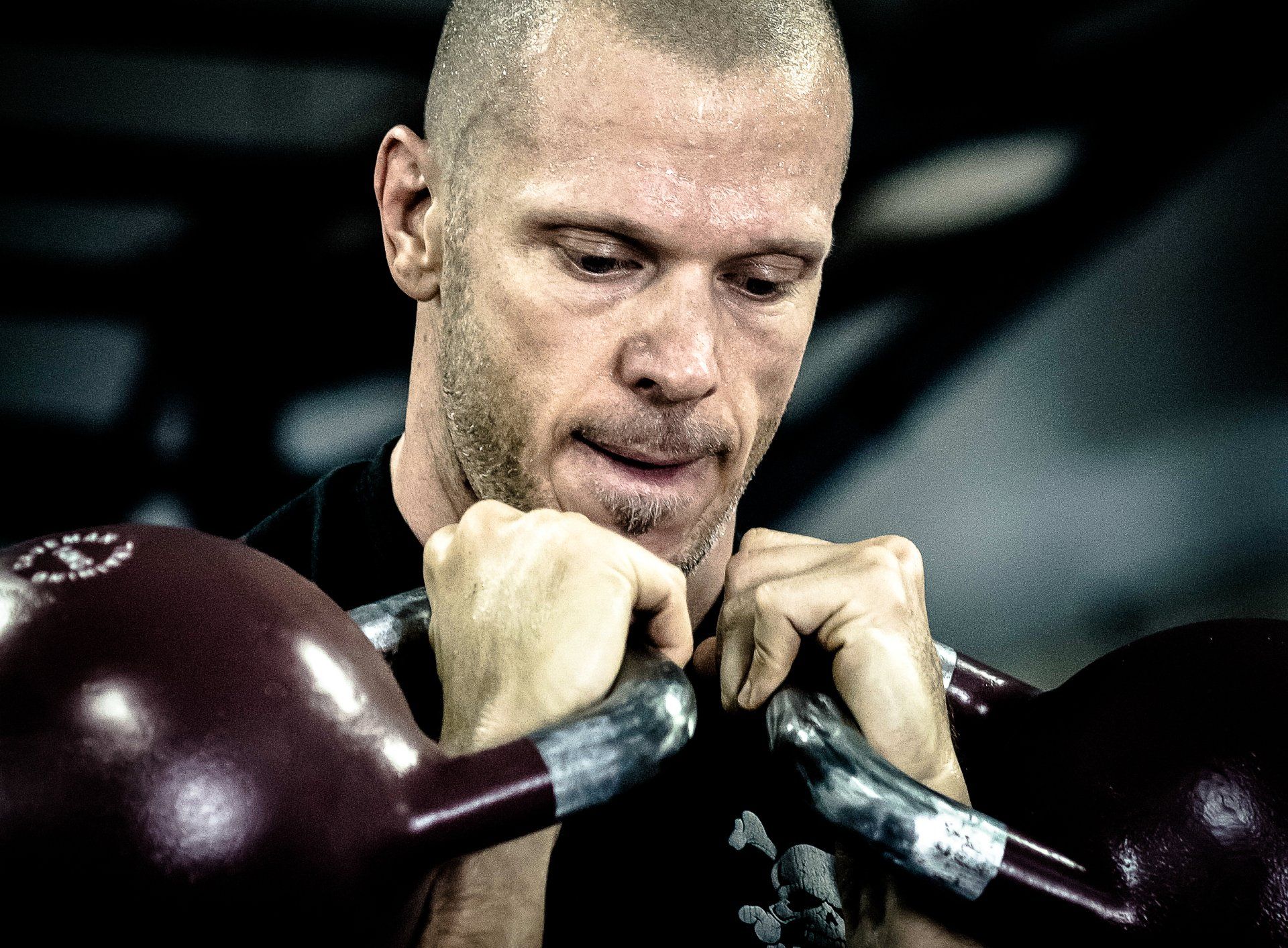 Man gripping two red kettlebells, focused expression, gym setting.
