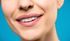 Close-up of a person smiling, showing white teeth and full lips against a blue background.