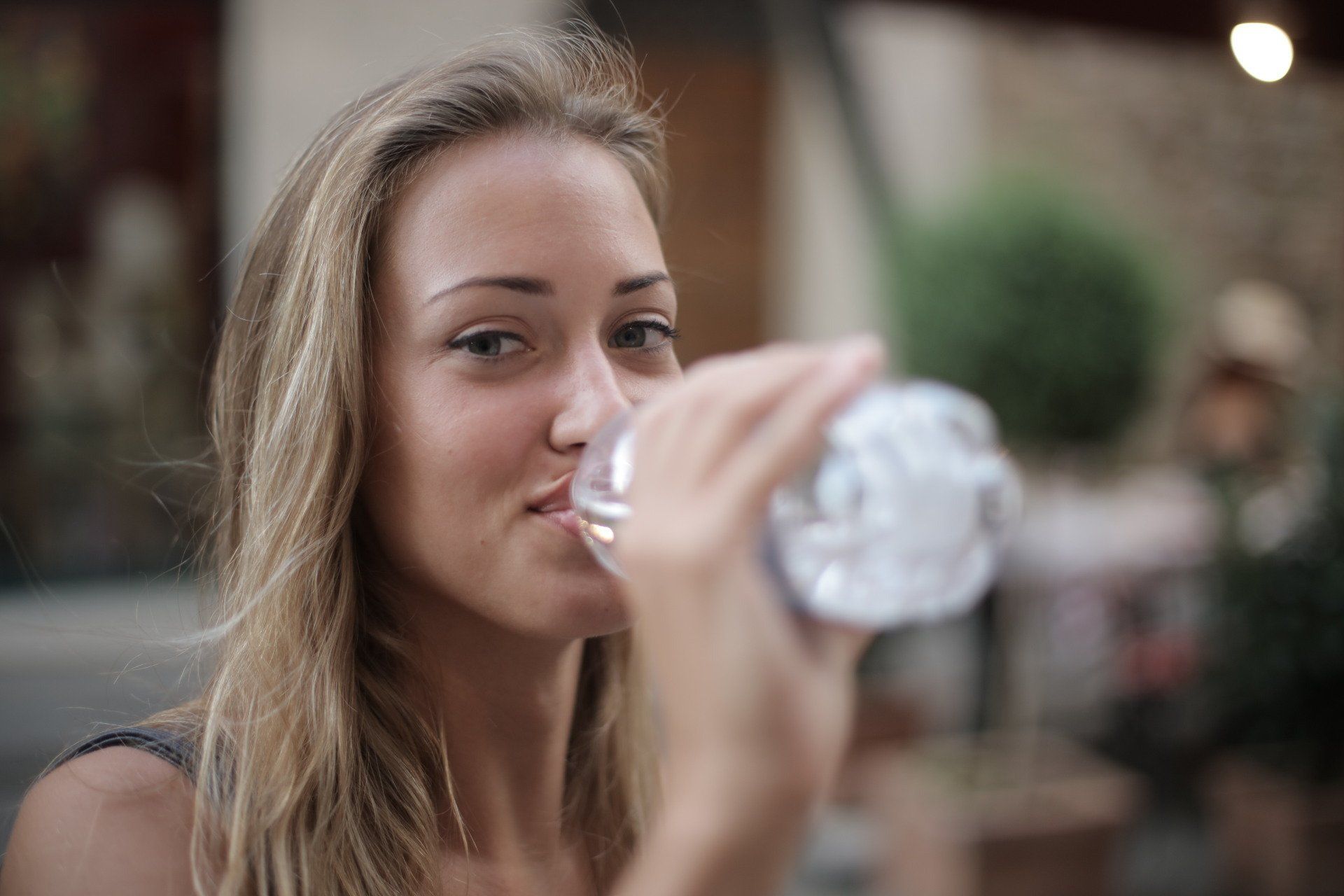 A woman is drinking water from a plastic bottle.