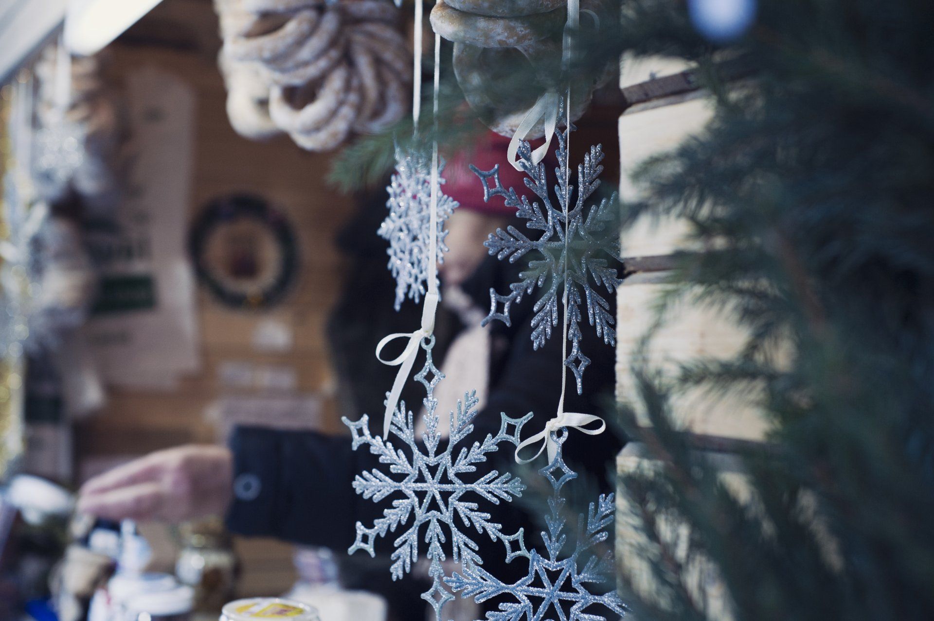 Decorative snowflakes hang in front of a blurred wooden market stall with evergreen branches.