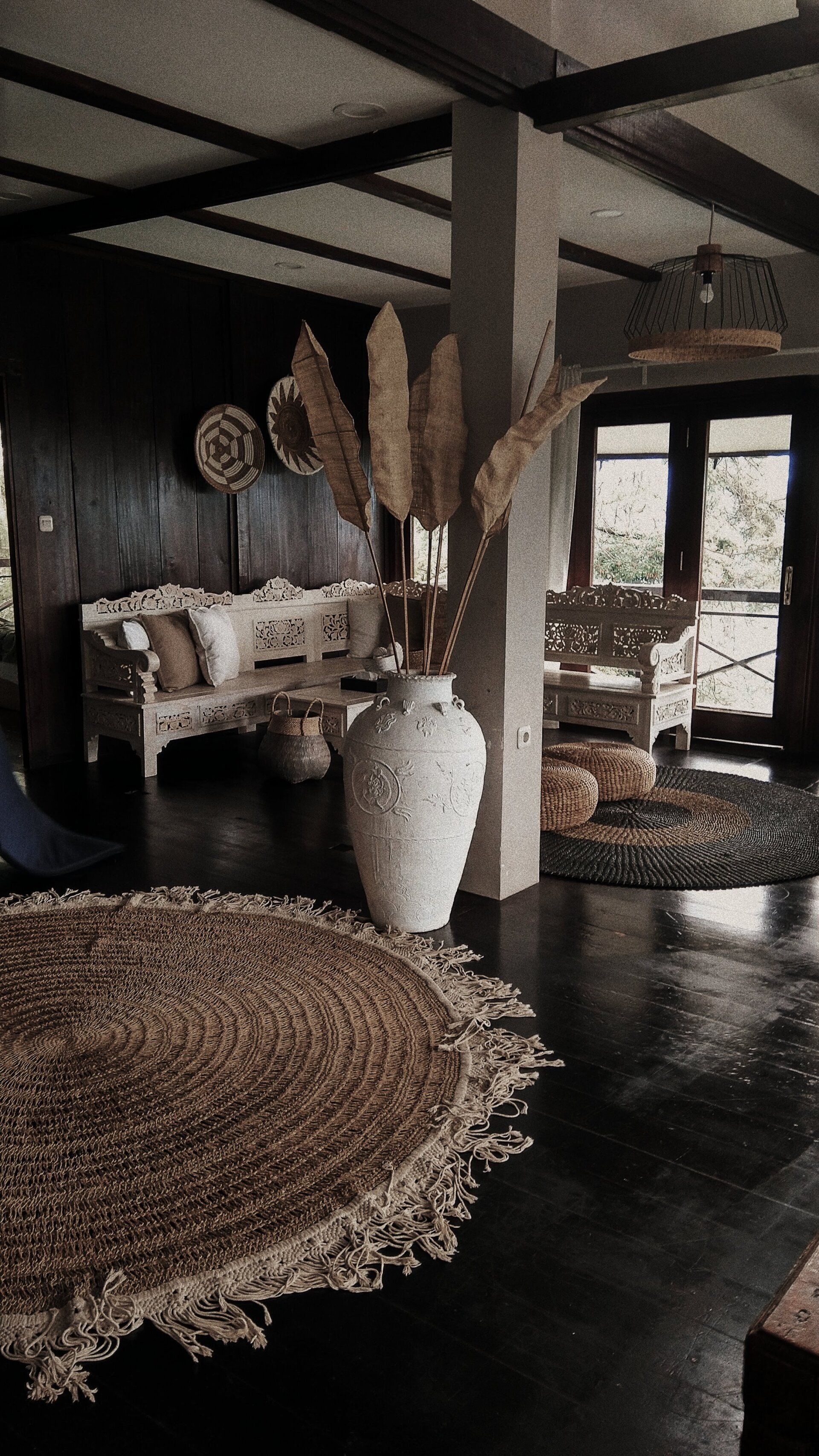 Interior with dark wood, white seating, large vase with dried florals, round rug.