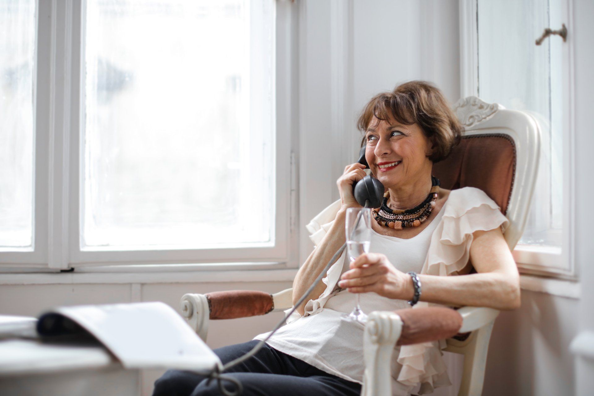 Woman smiling while talking on a phone in a bright office chair near a window
