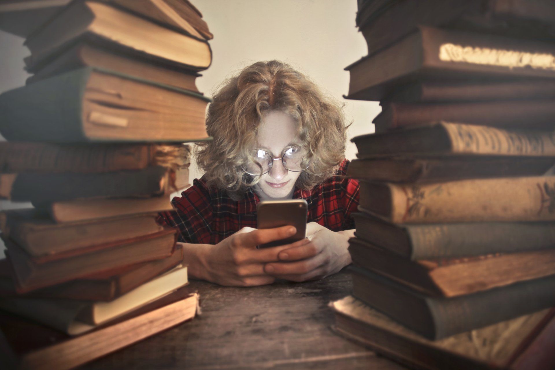 Person reading a phone between tall stacks of books on a table