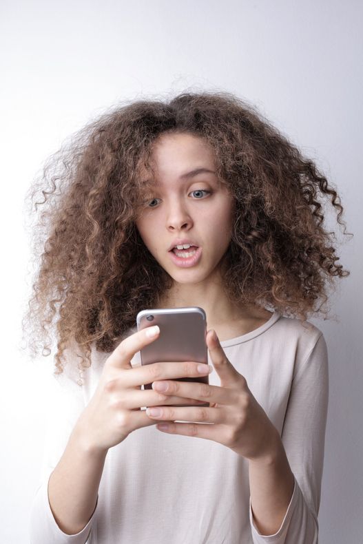 Person with curly hair looking at a smartphone against a light background