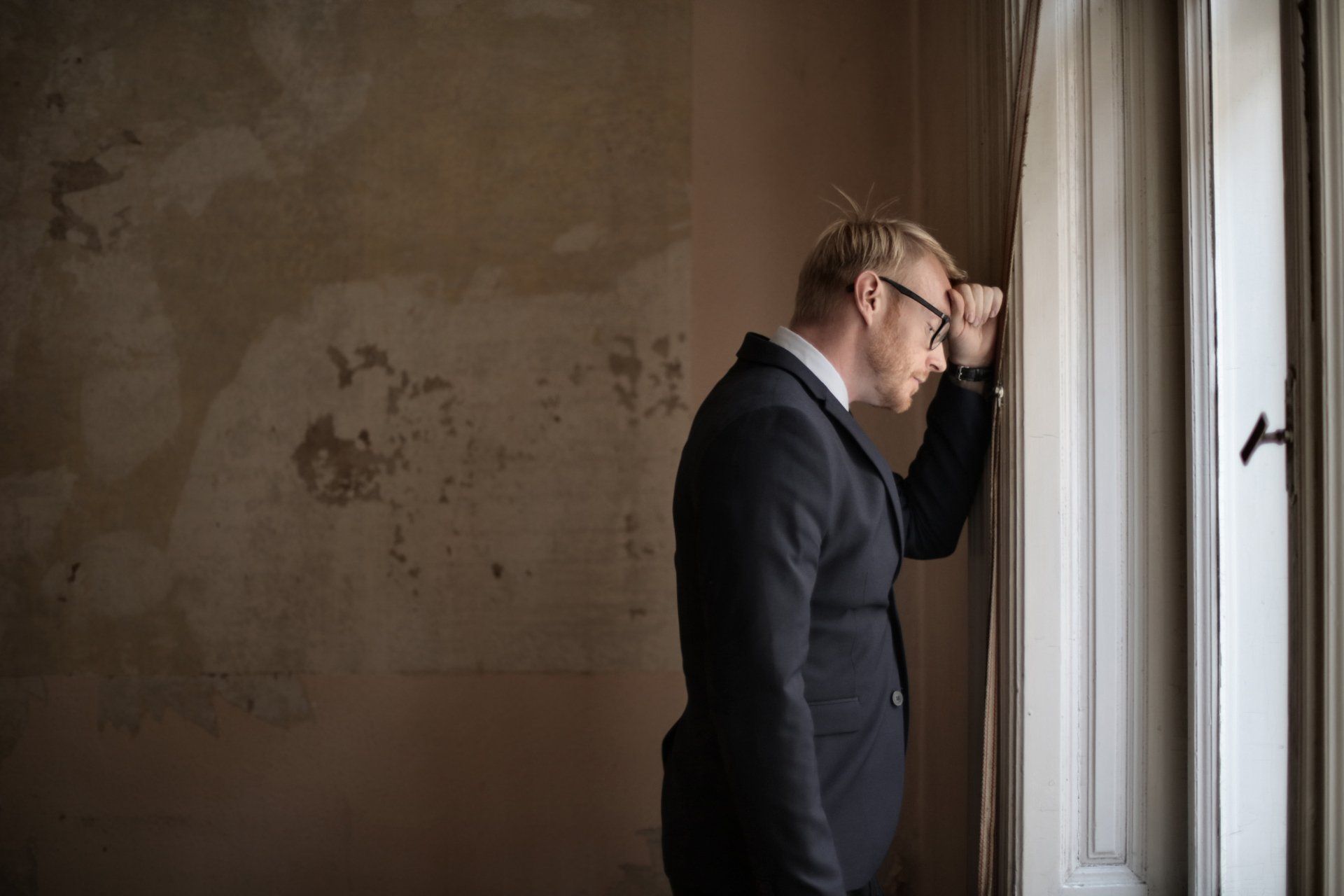 A man in a suit and tie is leaning against a window.