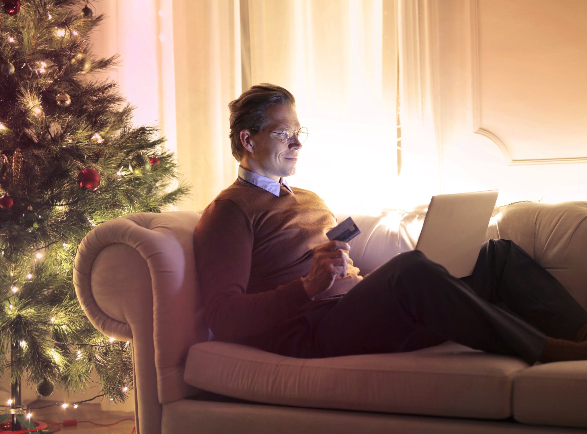A man is sitting on a couch using a laptop and a credit card.